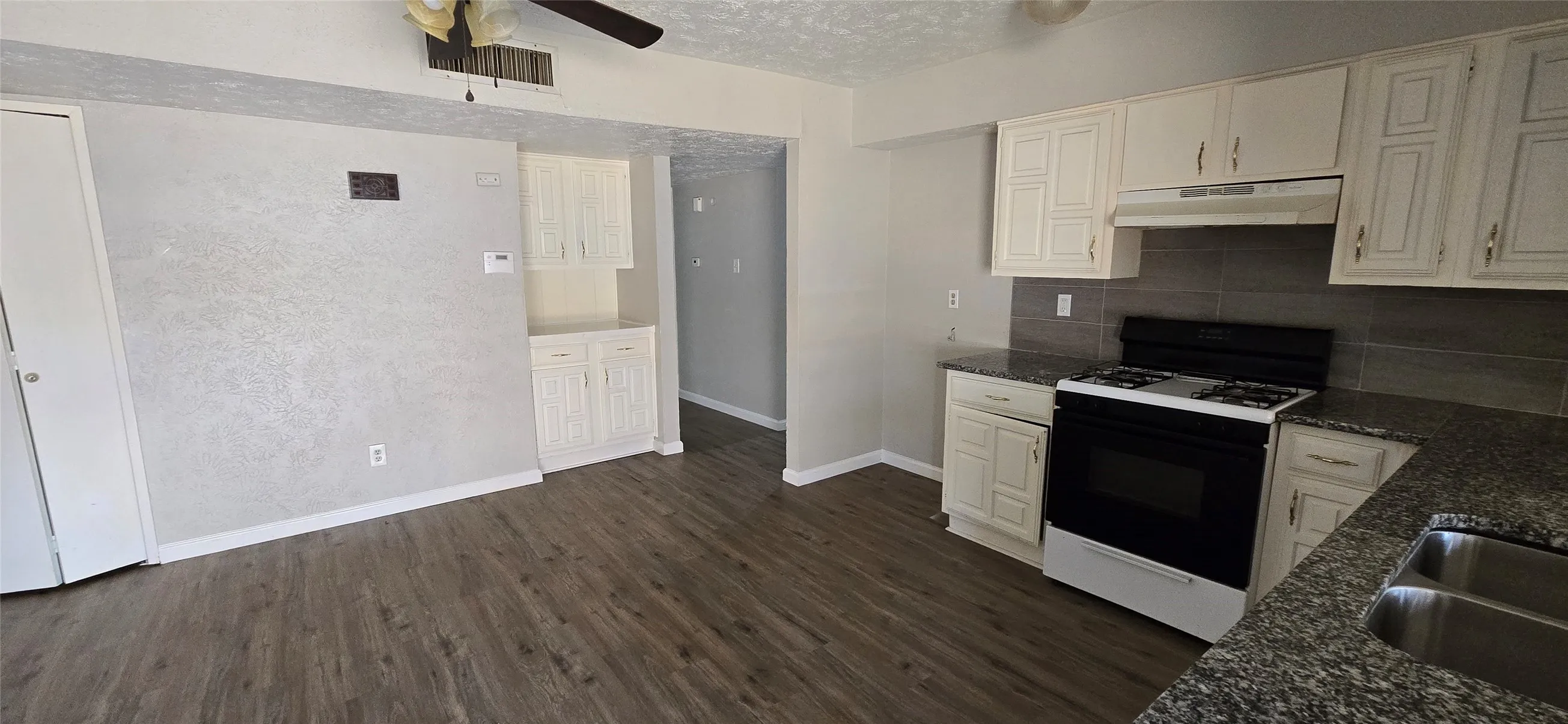 Kitchen area featuring light-colored cabinetry, dark granite-look countertops, stainless steel sink, and a black range
