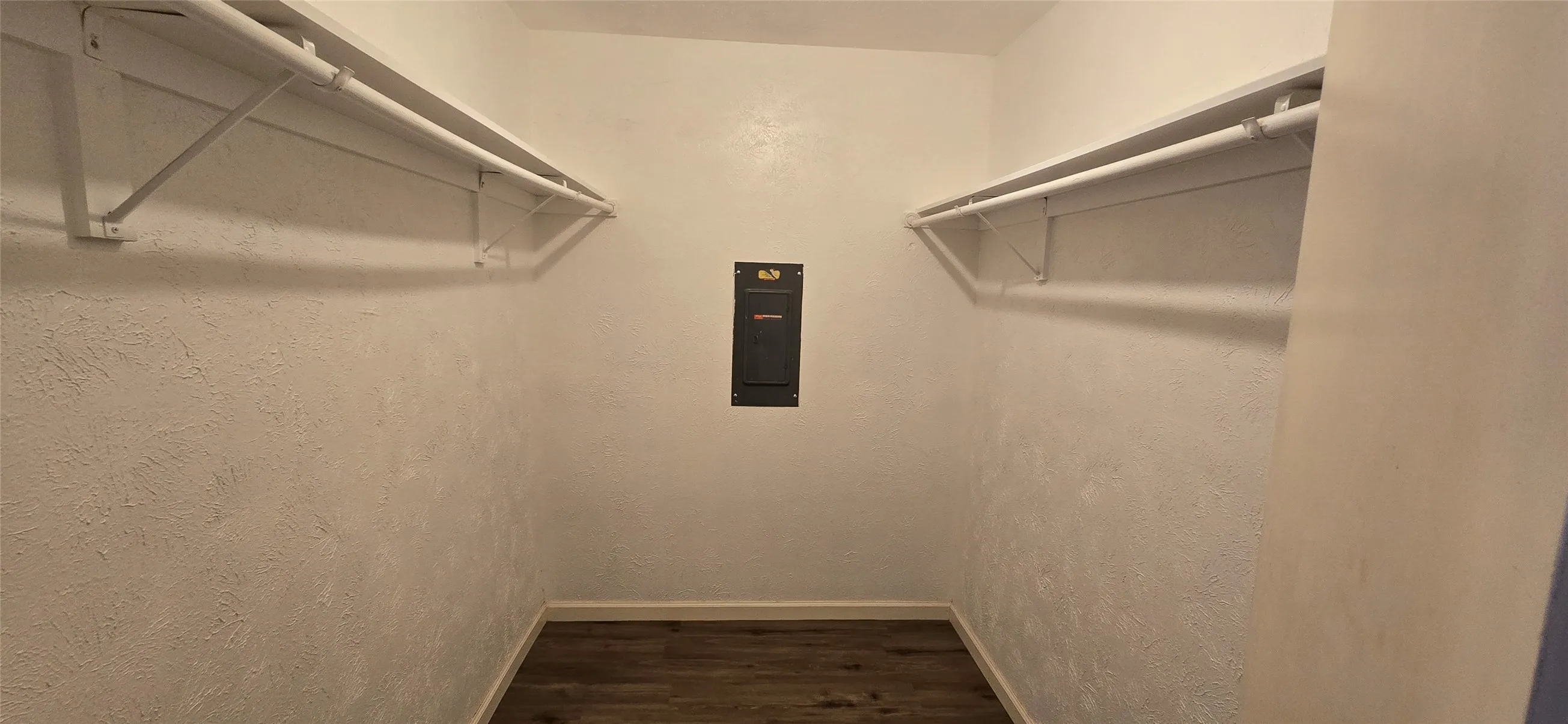 Closet featuring wood-finish flooring, white textured walls, and dual clothing rods with shelving