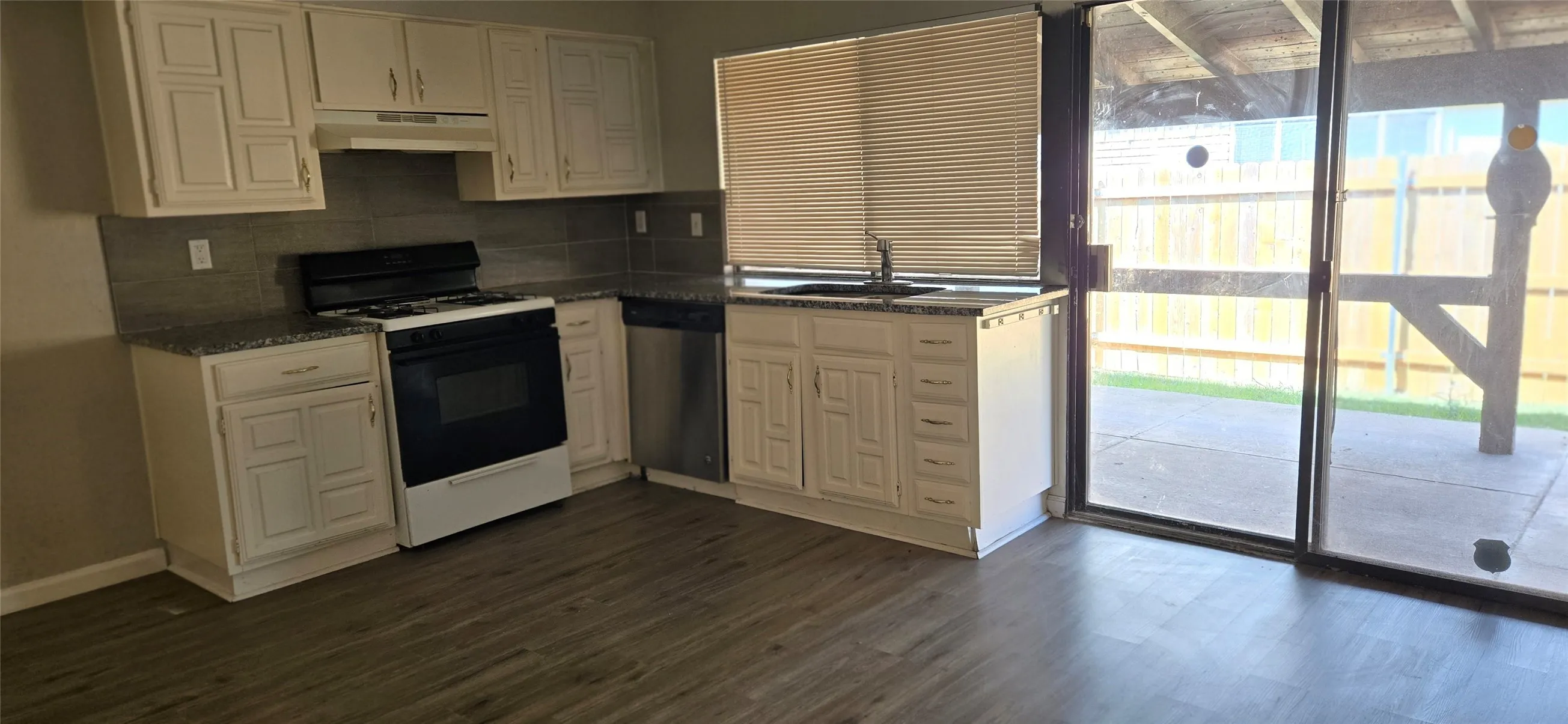 Kitchen featuring white cabinetry, dark granite-style countertops, and a gray subway tile backsplash