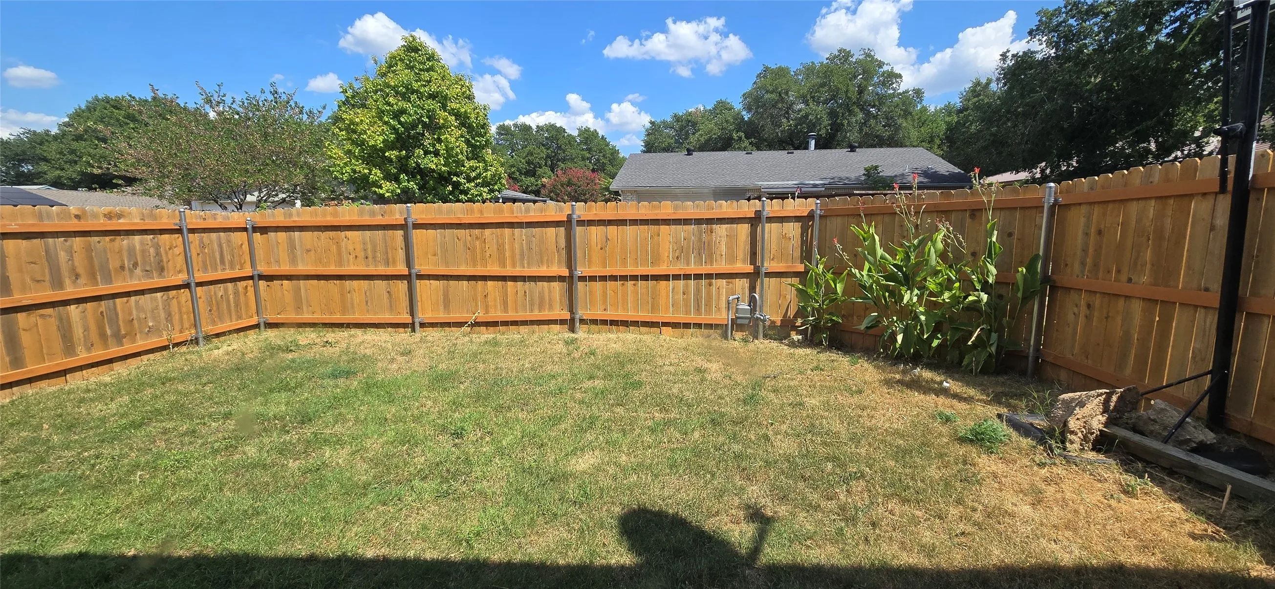 Fenced backyard featuring a wood privacy fence and a grassy lawn