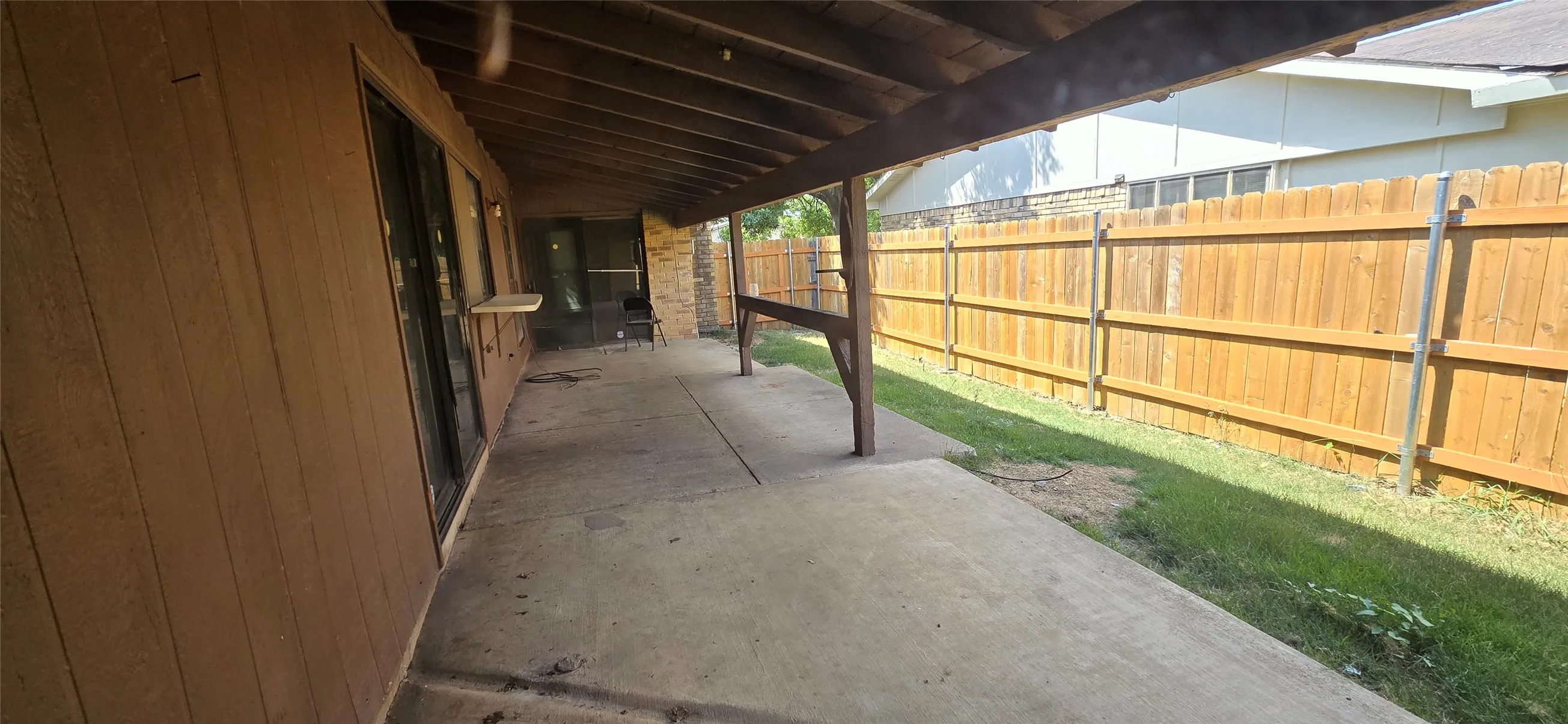 Expansive covered patio featuring a concrete slab, exposed wood beam ceiling, and a wooden privacy fence