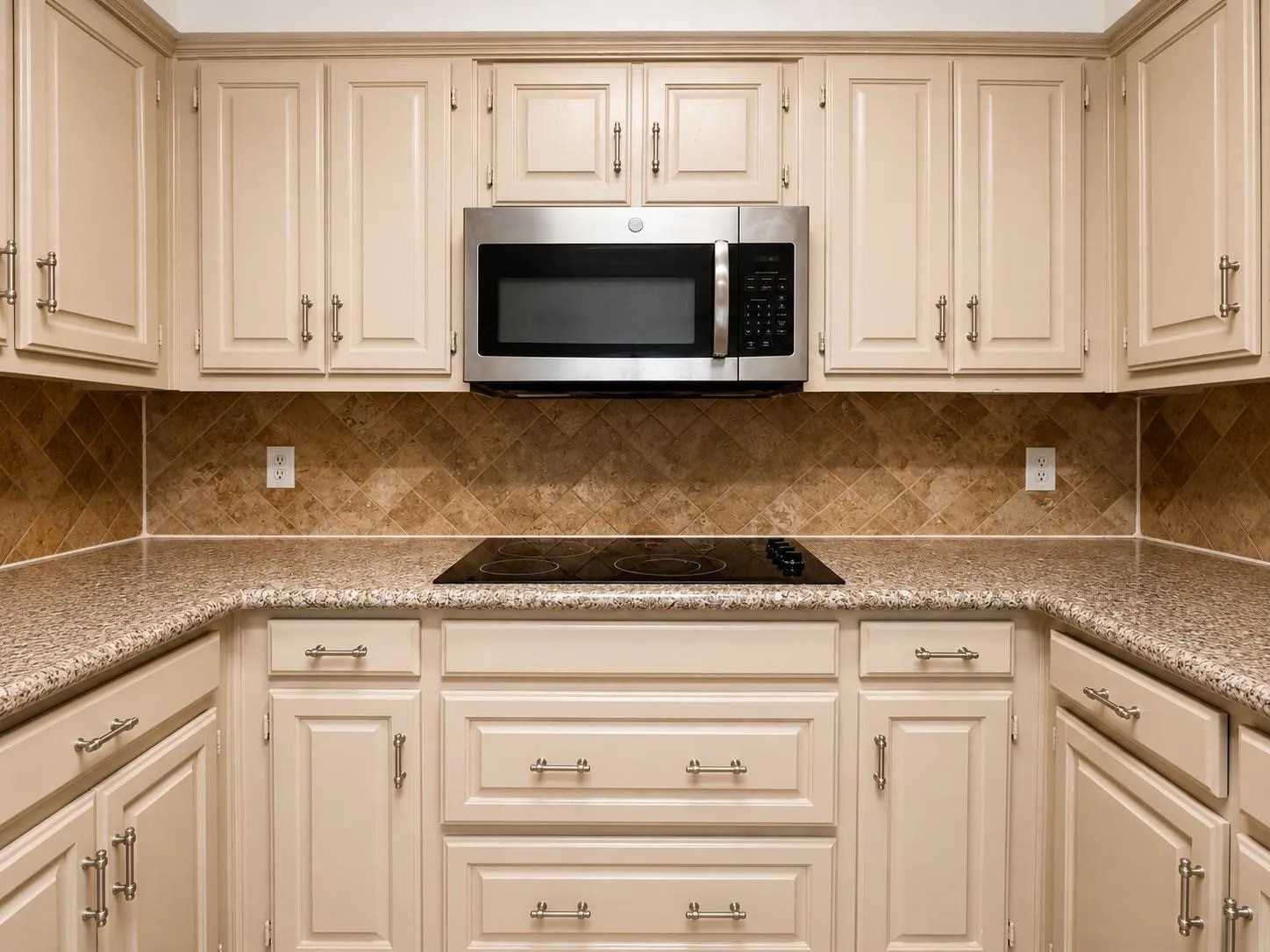 Kitchen featuring cream-colored cabinetry with brushed nickel hardware, a built-in stainless steel microwave, a black electric cooktop, and speckled countertops