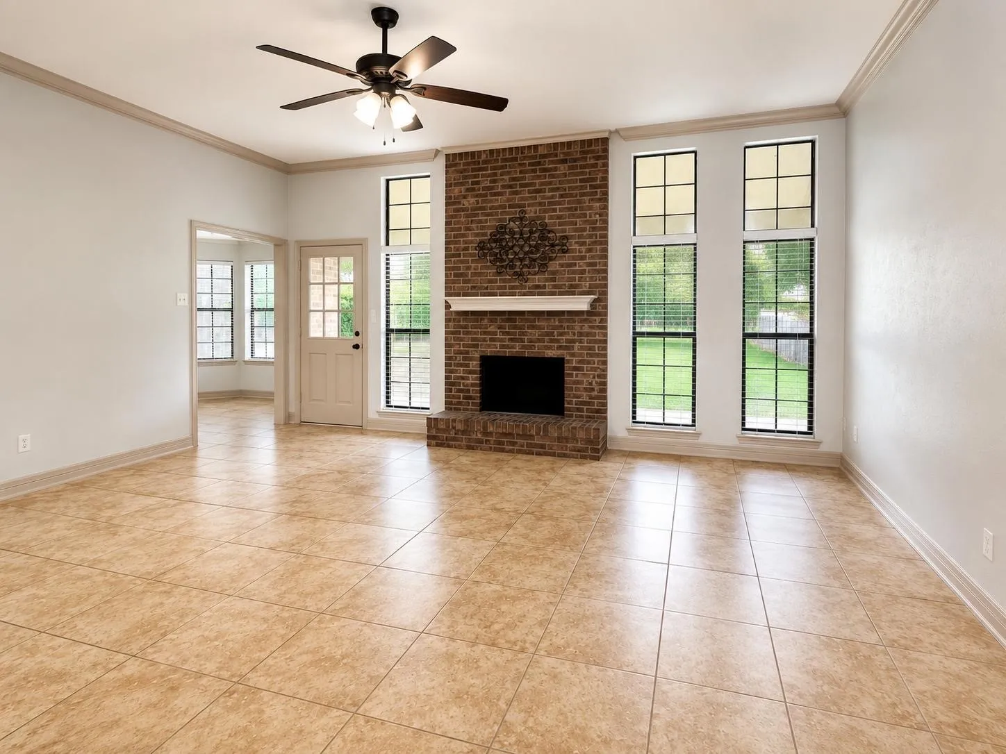Living space featuring a brick fireplace with a white mantel, ceiling fan, and large tile flooring