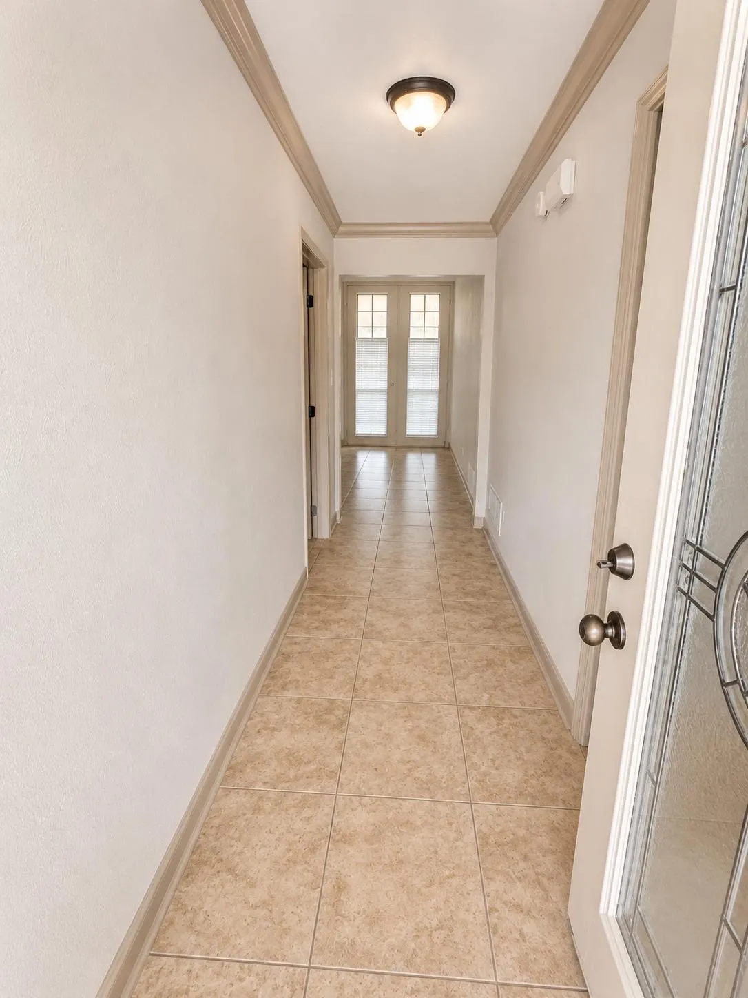 Entry hall featuring neutral-toned ceramic tile flooring, crown molding, and a flush-mount ceiling light