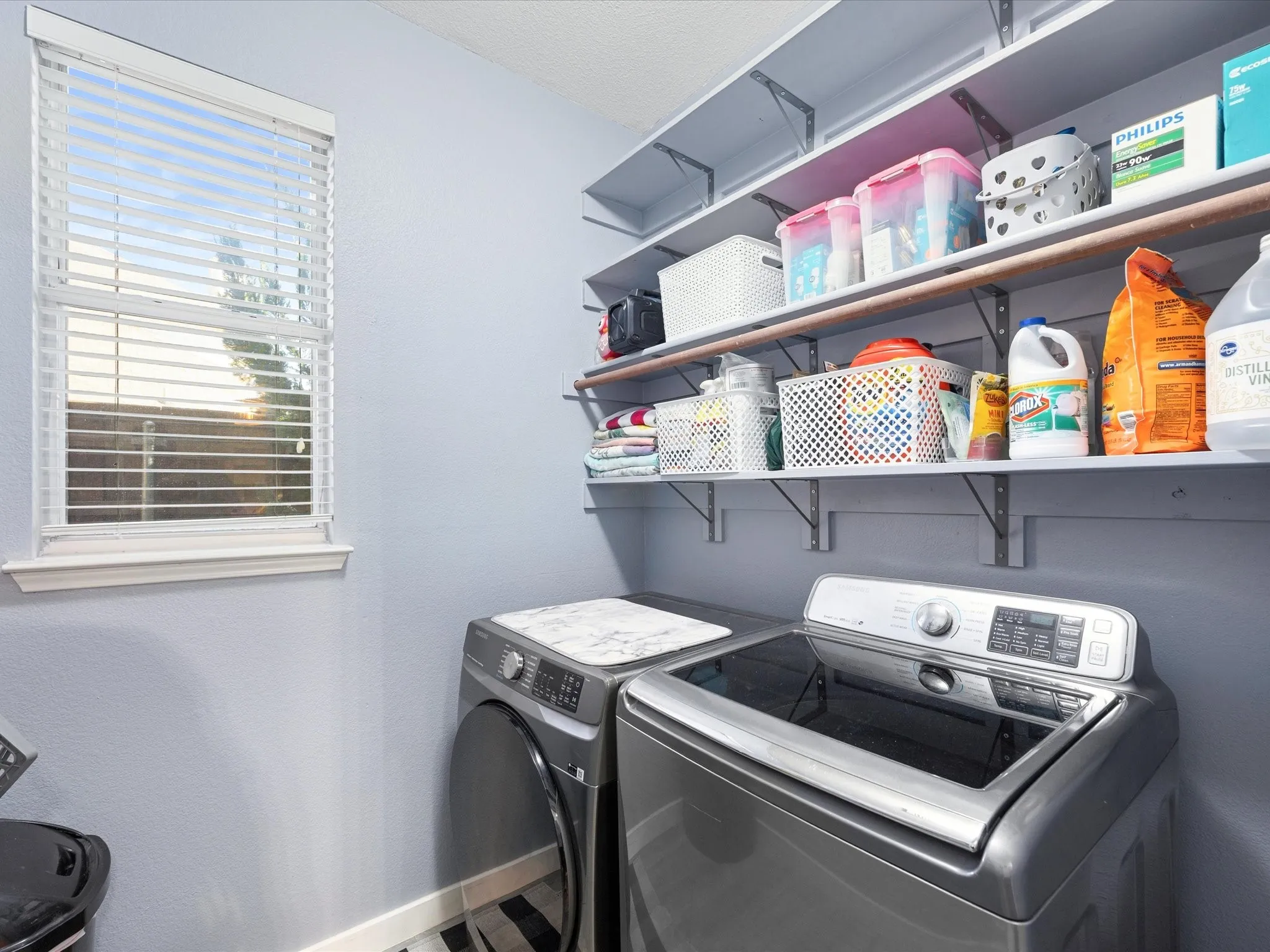 Utility space with extensive wall-mounted shelving, a window with horizontal blinds, and light blue walls