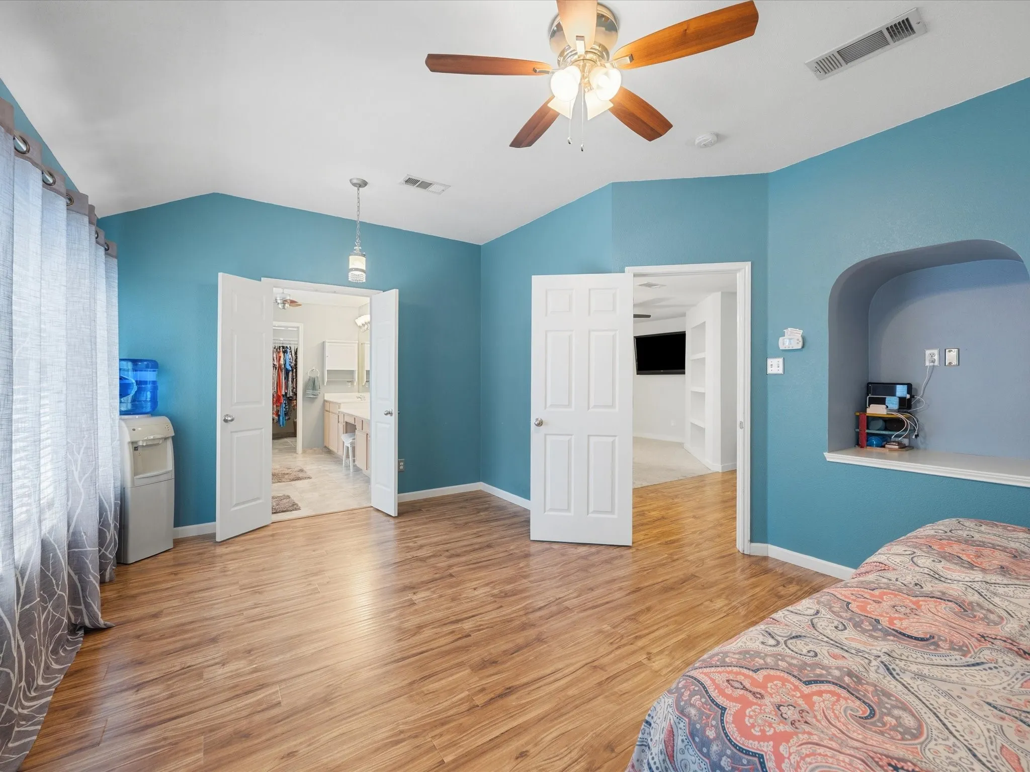 Spacious room featuring wood-finish flooring, a ceiling fan, and recessed shelving