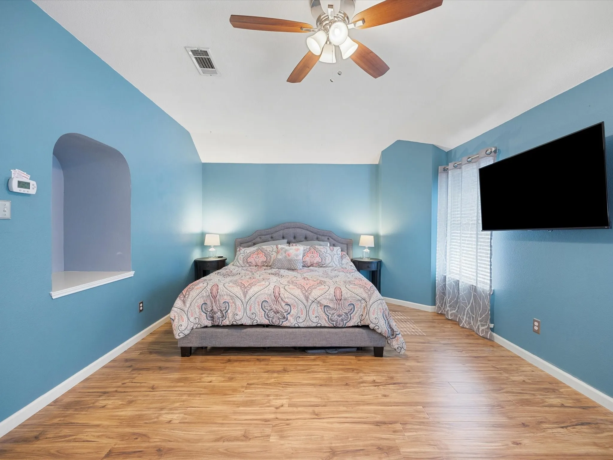 Spacious room featuring wood-finish flooring, vaulted ceiling, and a ceiling fan