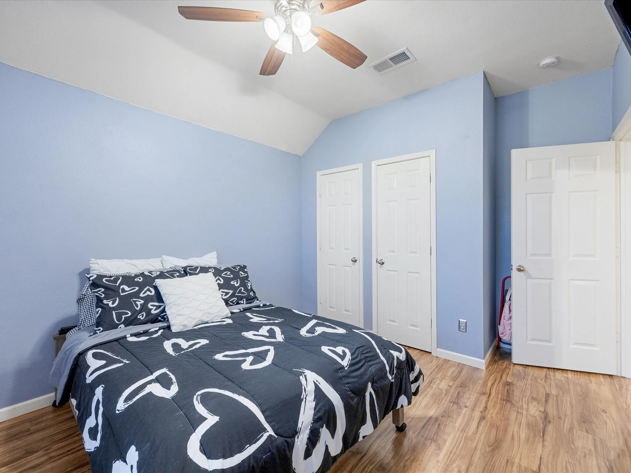 Interior room featuring wood-finish flooring, light blue painted walls, and a vaulted ceiling