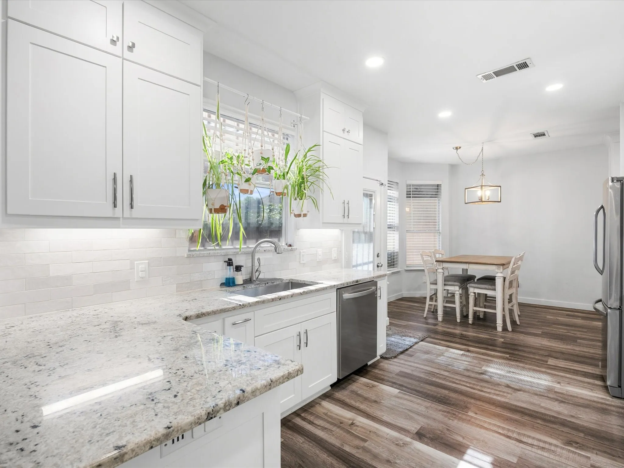 White shaker cabinetry with stone countertops, a subway tile backsplash, and wood-finish flooring