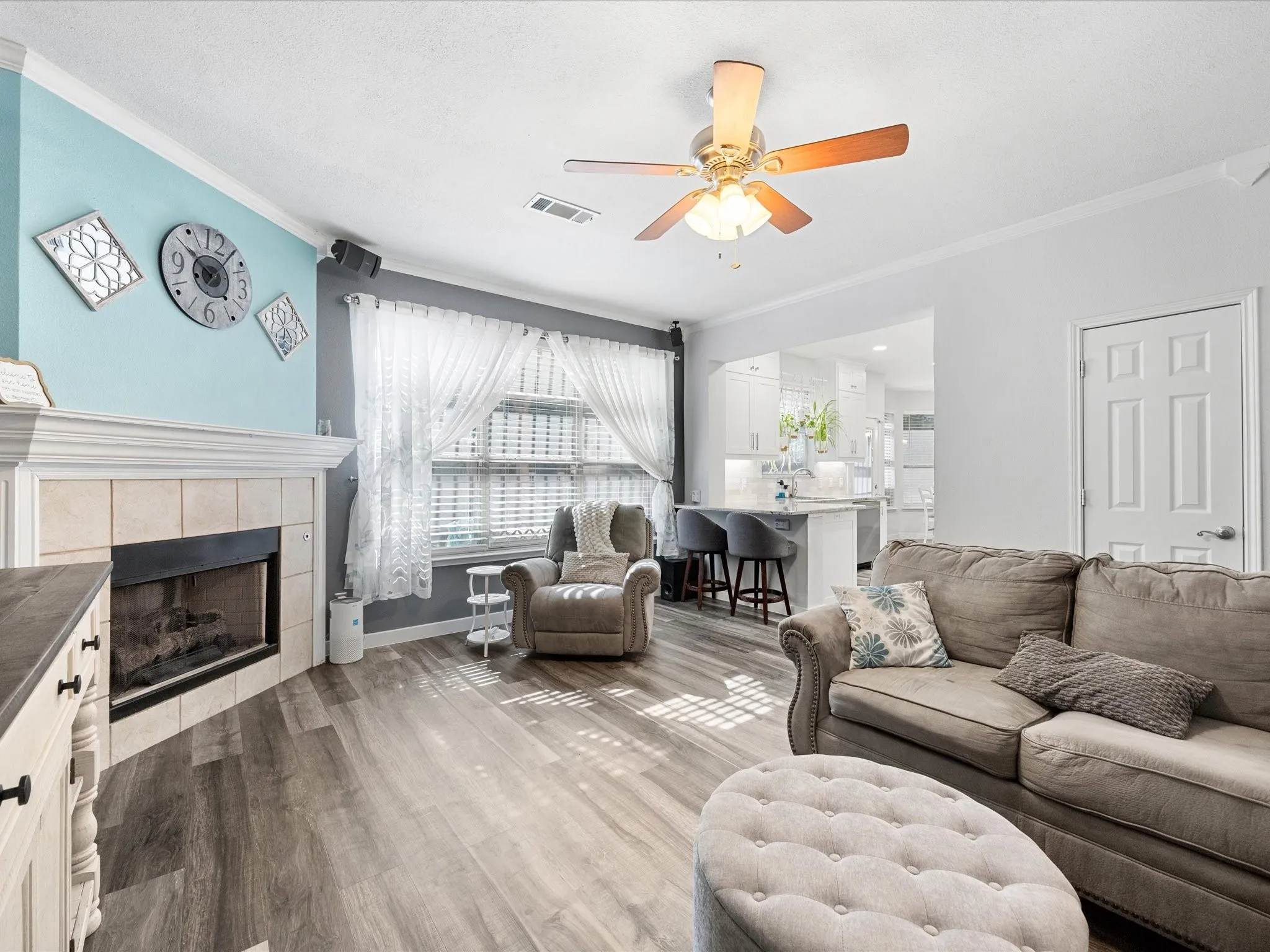 Living area featuring wood-finish flooring, a ceiling fan, crown molding, and a tiled fireplace
