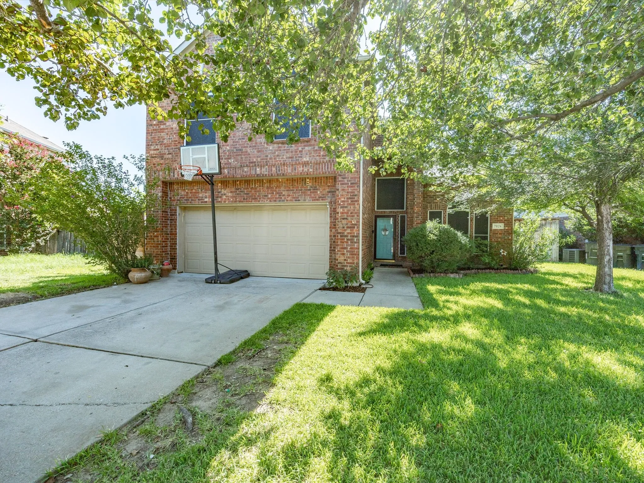 Brick facade home featuring a two-car garage, established front yard, mature trees, and a concrete driveway