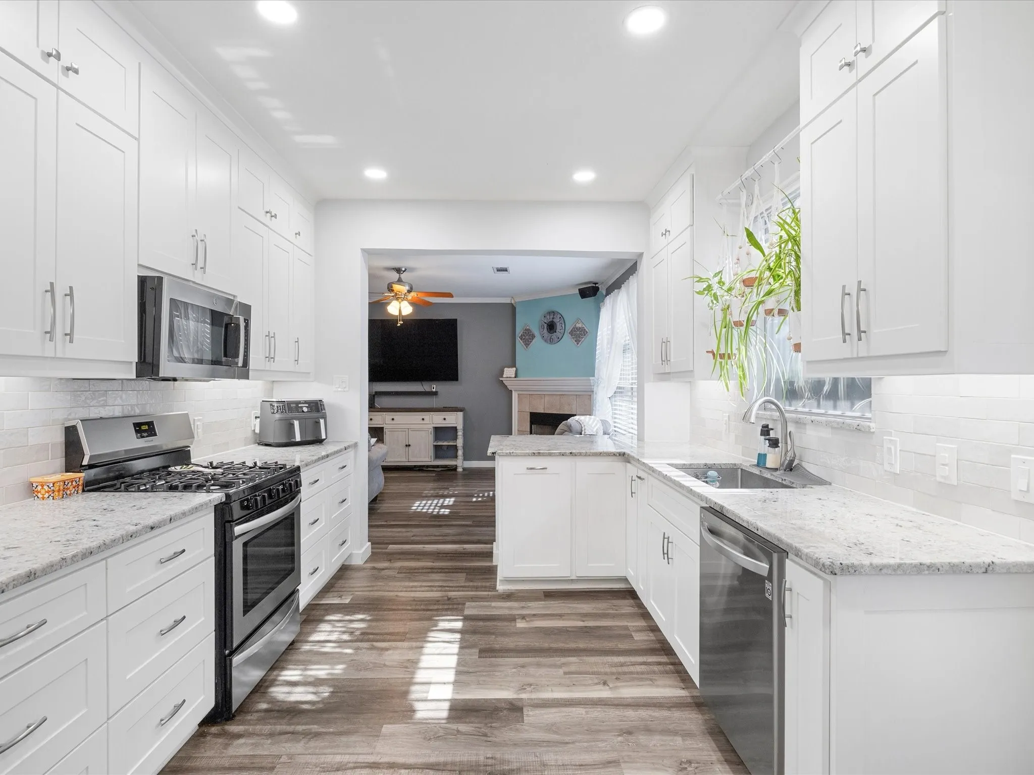 Bright kitchen featuring extensive white shaker cabinetry, stainless steel appliances, granite-style countertops, wood-finish flooring, and a white subway tile backsplash