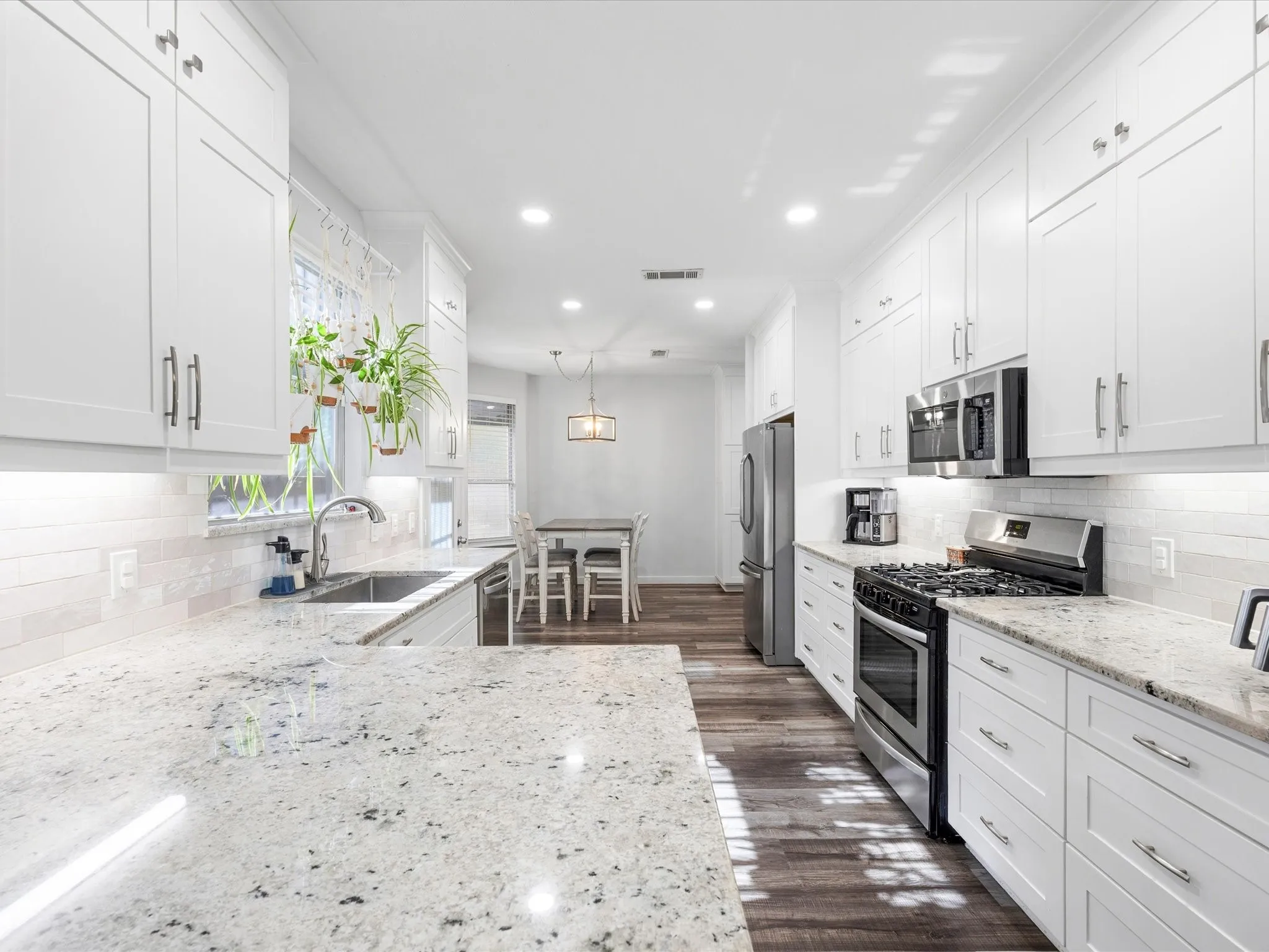 Galley kitchen featuring abundant white cabinetry, stainless steel appliances, granite countertops, and wood-finish flooring