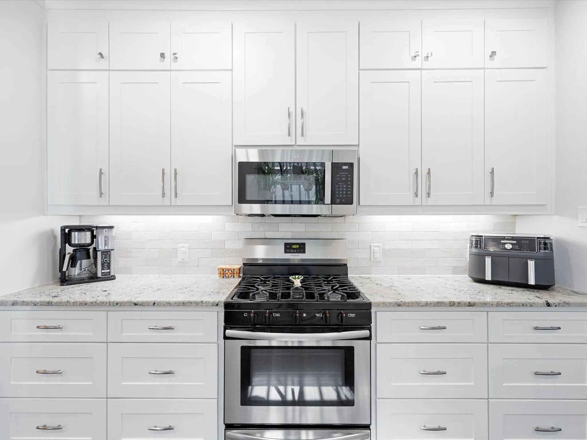 Contemporary kitchen featuring white shaker cabinetry, stainless steel range with gas cooktop, built-in stainless steel microwave, speckled countertops, and a white subway tile backsplash