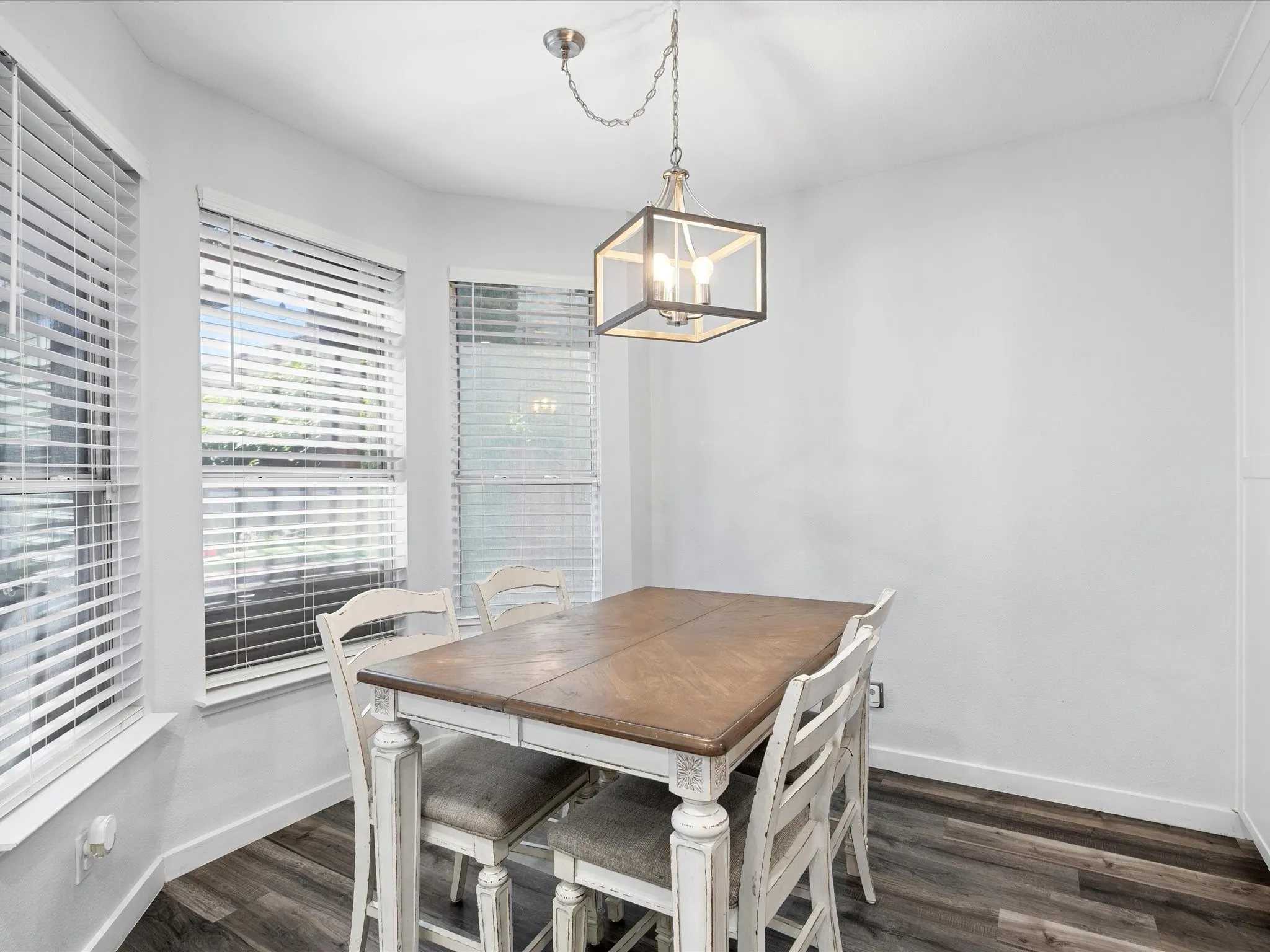 Dining area featuring an industrial-style chandelier, three large windows with blinds, white walls, and wood-finish flooring