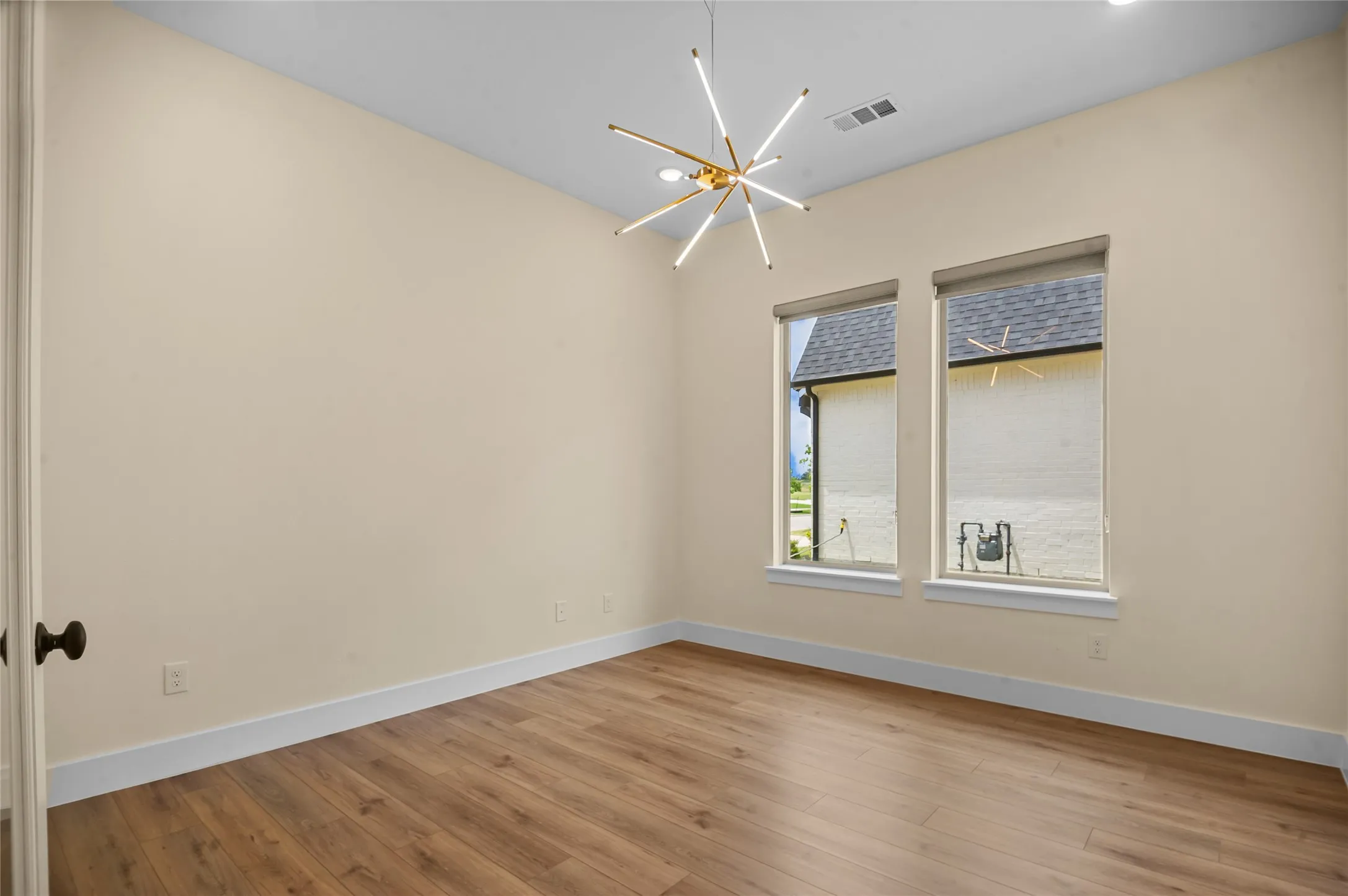 Spacious room featuring high ceilings, contemporary light fixture, wood-finish flooring, and two windows with roller shades