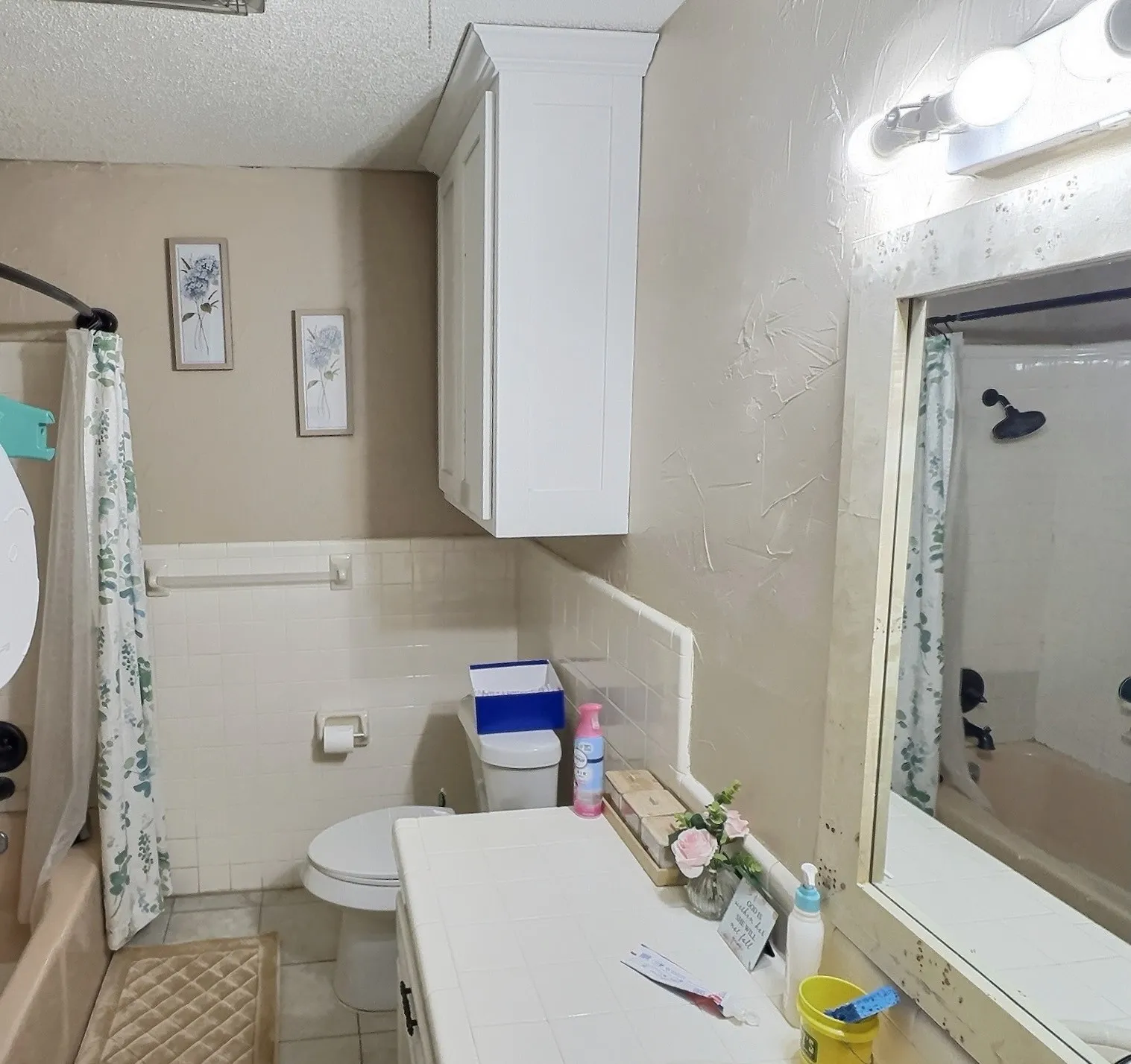 Bathroom featuring a white vanity with tile countertop, white wall-mounted cabinetry, white tiled tub surround, and neutral wall tones