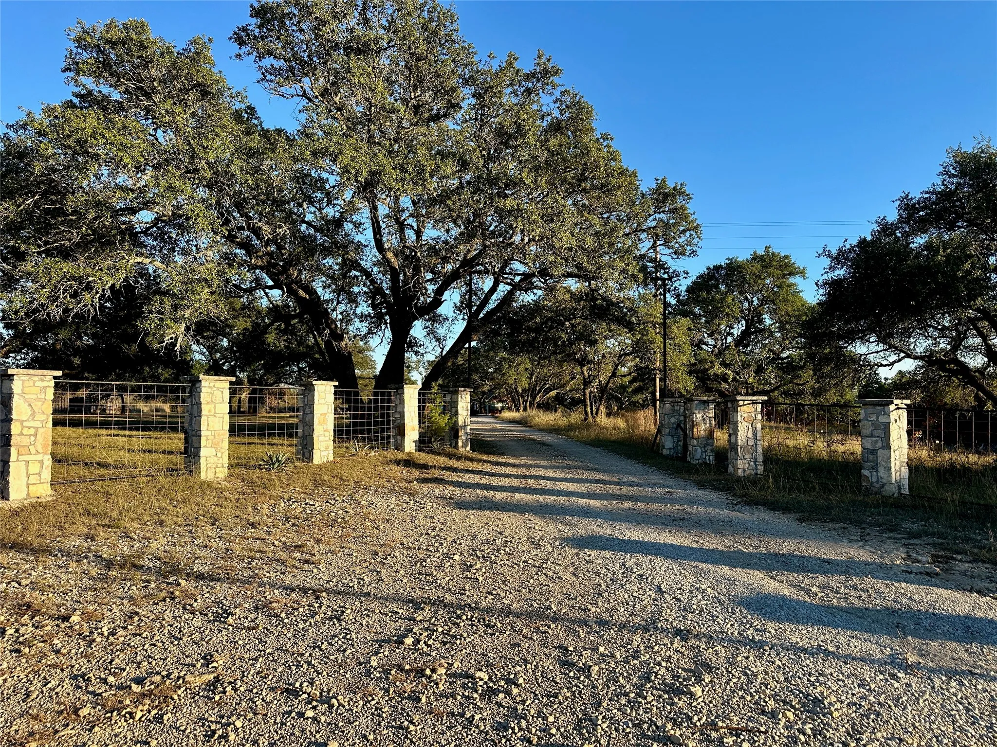 Gravel drive with stone pillars, metal fencing, and mature trees lining the property