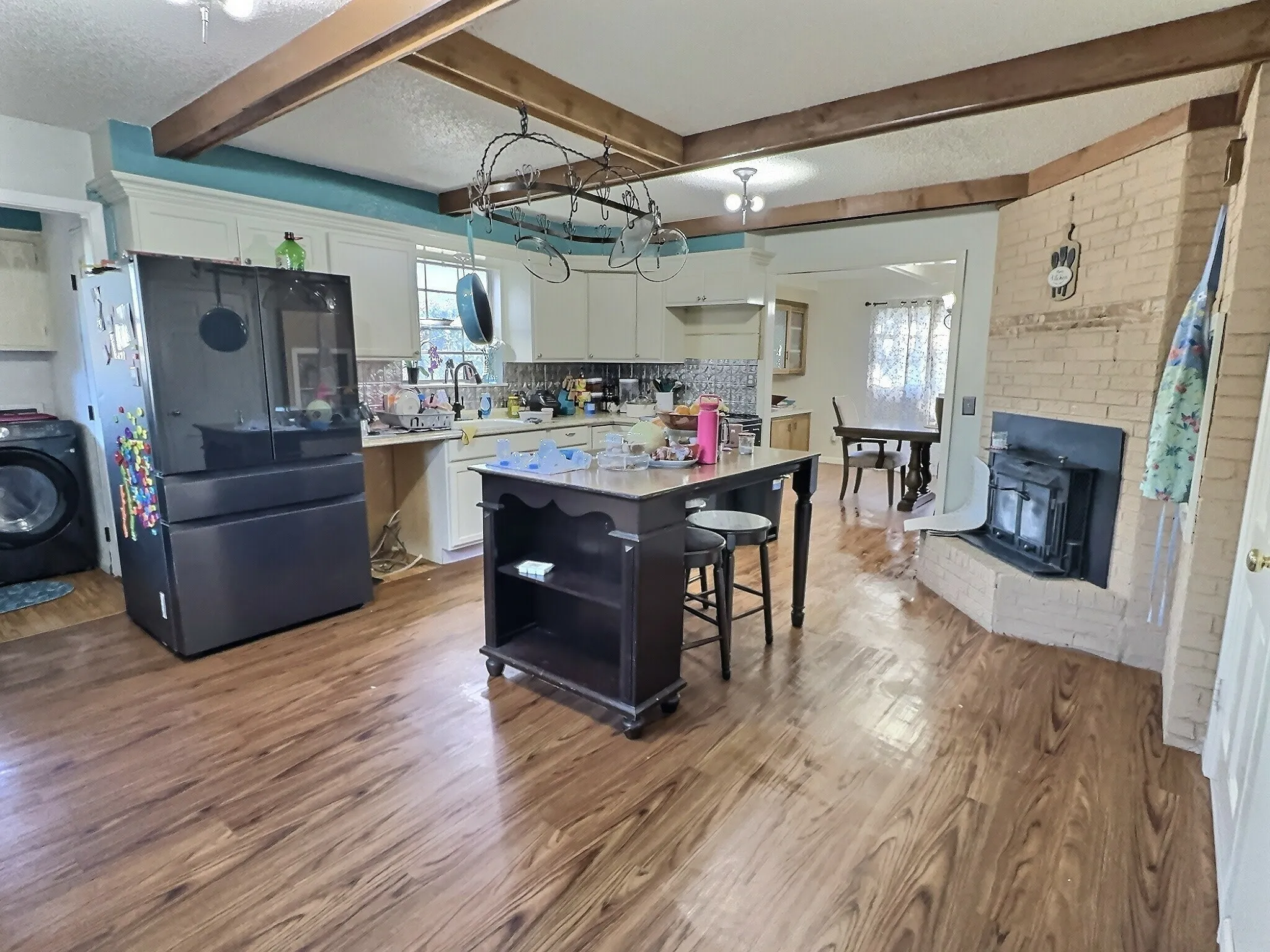 Spacious kitchen featuring wood-finish flooring, white cabinetry, a central island, and a brick fireplace with an insert