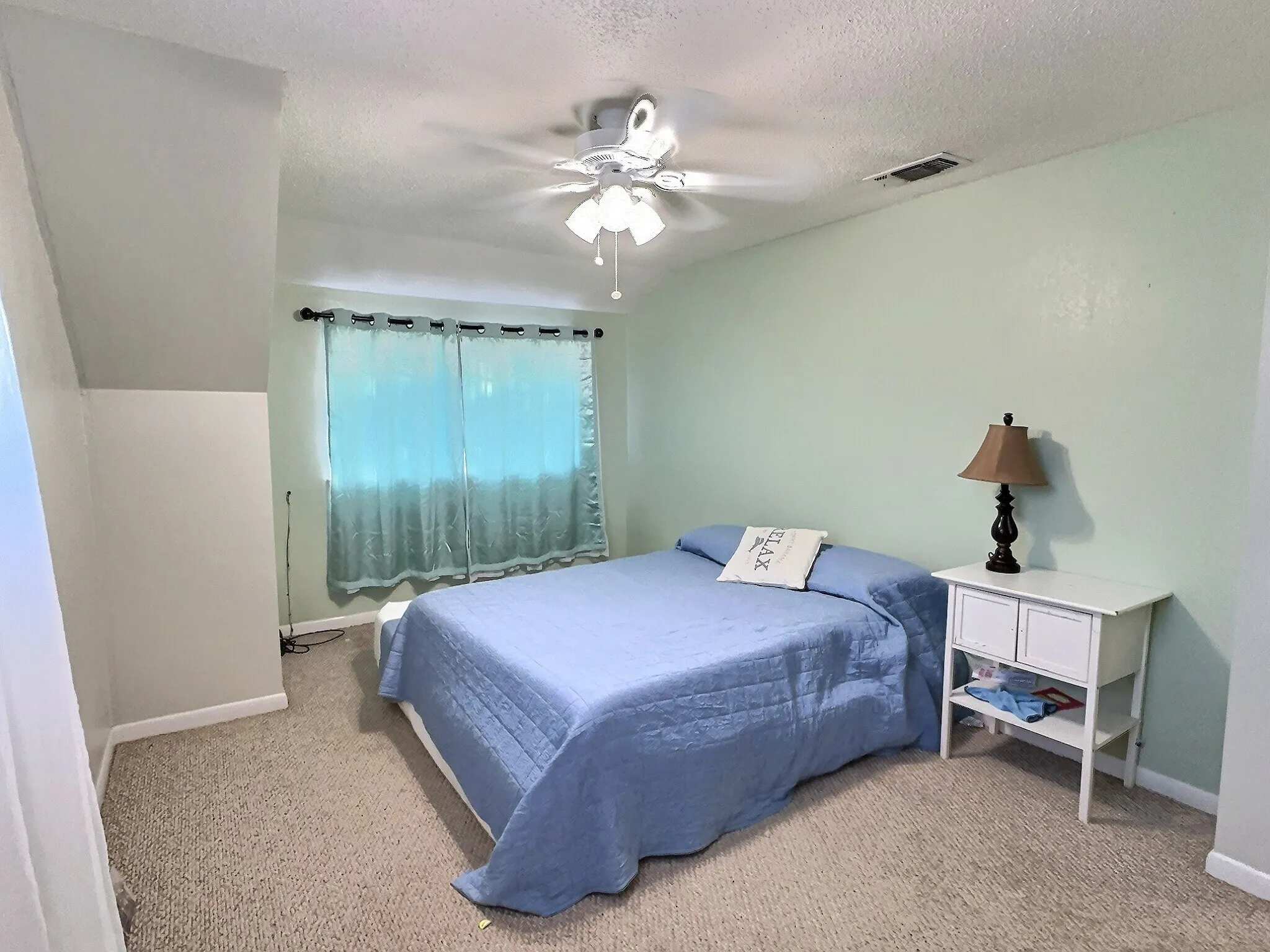 Bedroom featuring light green walls, textured carpet flooring, and a ceiling fan with integrated lighting