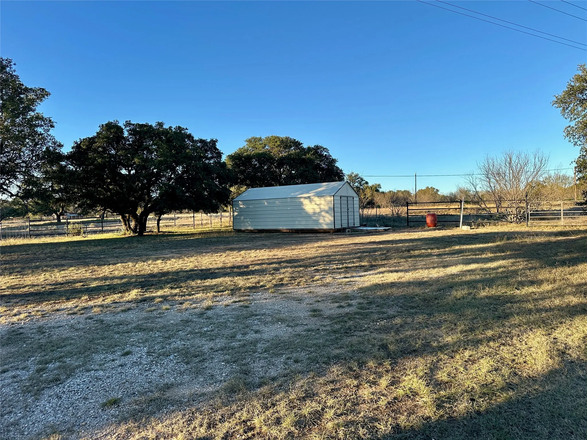 Expansive outdoor area featuring a storage shed, mature trees, and perimeter fencing