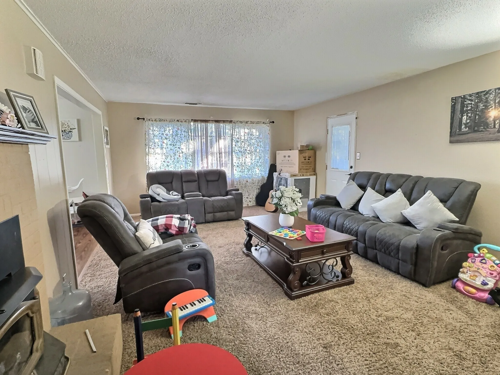 Spacious living area featuring neutral wall paint, textured carpeting, crown molding, and a prominent window