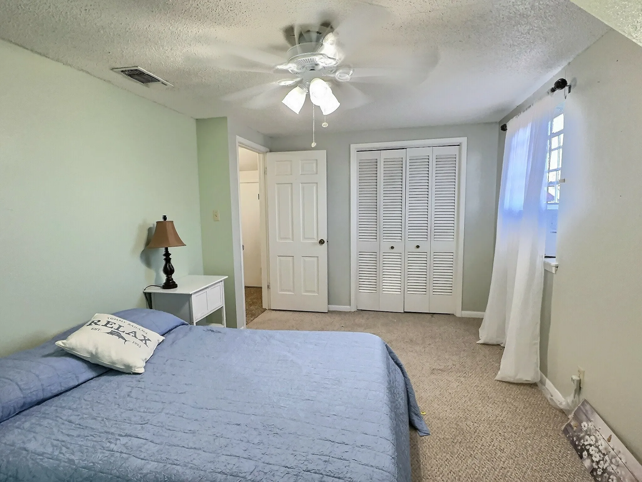 Carpeted room featuring a ceiling fan with integrated lighting, louvered bi-fold closet doors, and a window with white trim