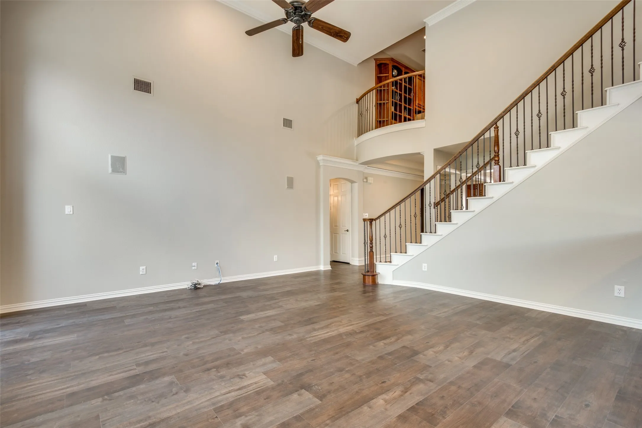 Soaring ceilings with a decorative fan fixture, wood-finish flooring, and a grand staircase featuring wrought iron balusters