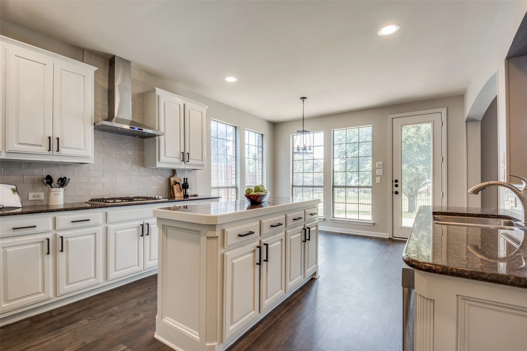 Kitchen featuring a central island, white cabinetry with dark hardware, dark countertops, and wood-finish flooring