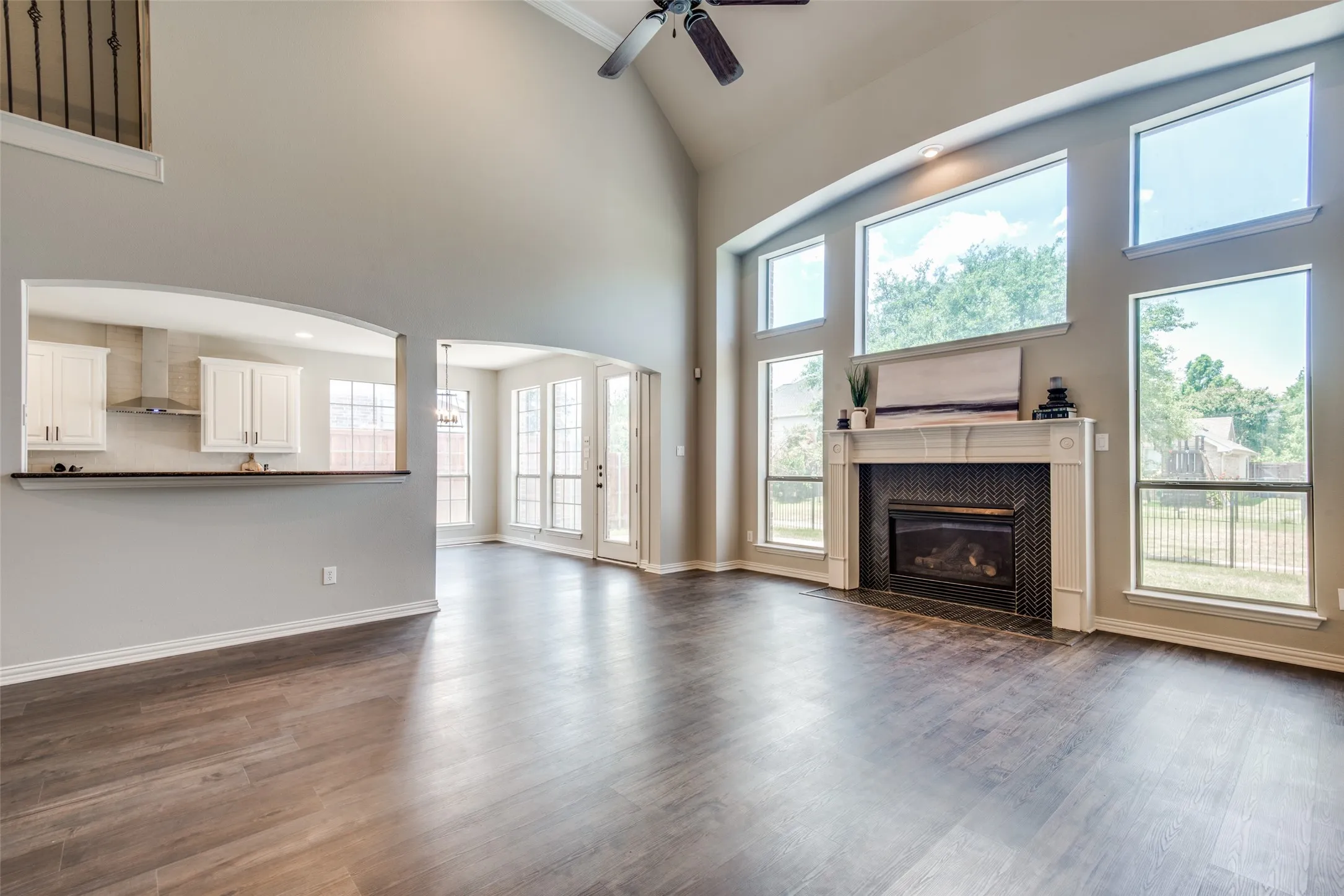Open-concept living area featuring high vaulted ceilings, wood-finish flooring, and a fireplace with a decorative mantel and dark tile surround