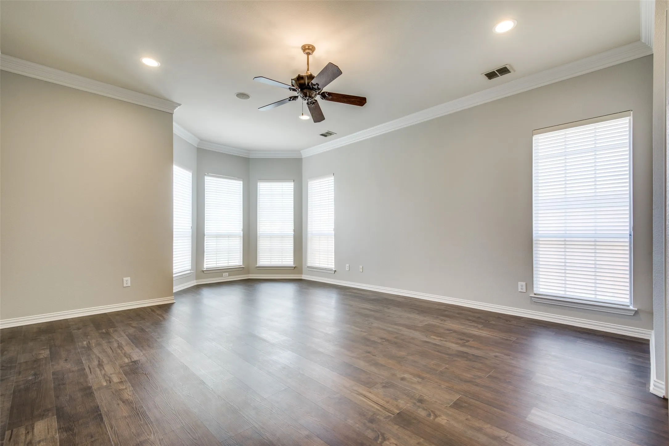 Spacious room featuring wood-finish flooring, a bay window configuration, crown molding, a ceiling fan, and recessed lighting