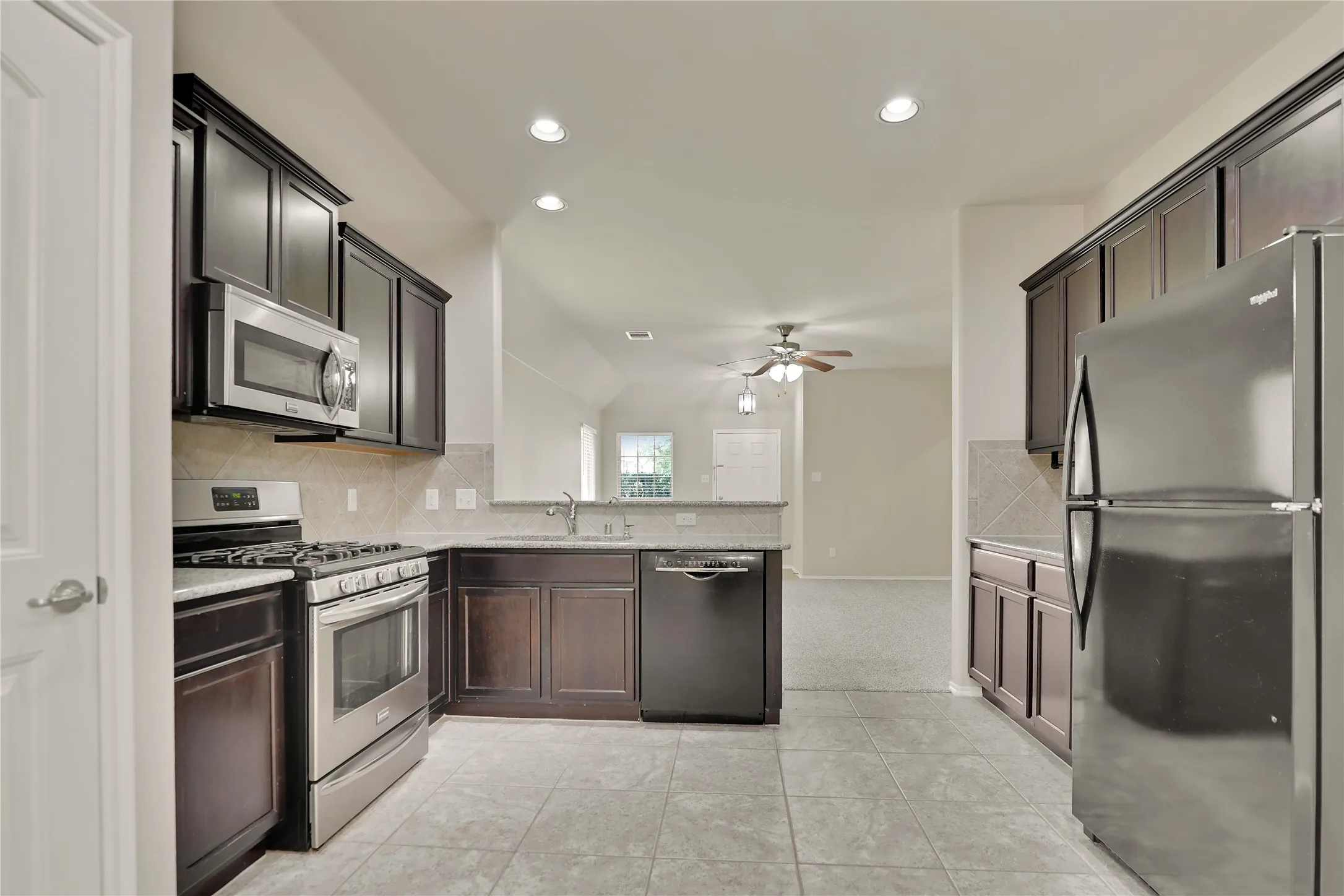 Kitchen featuring dark wood cabinetry, stainless steel appliances, granite-look countertops, and tile flooring