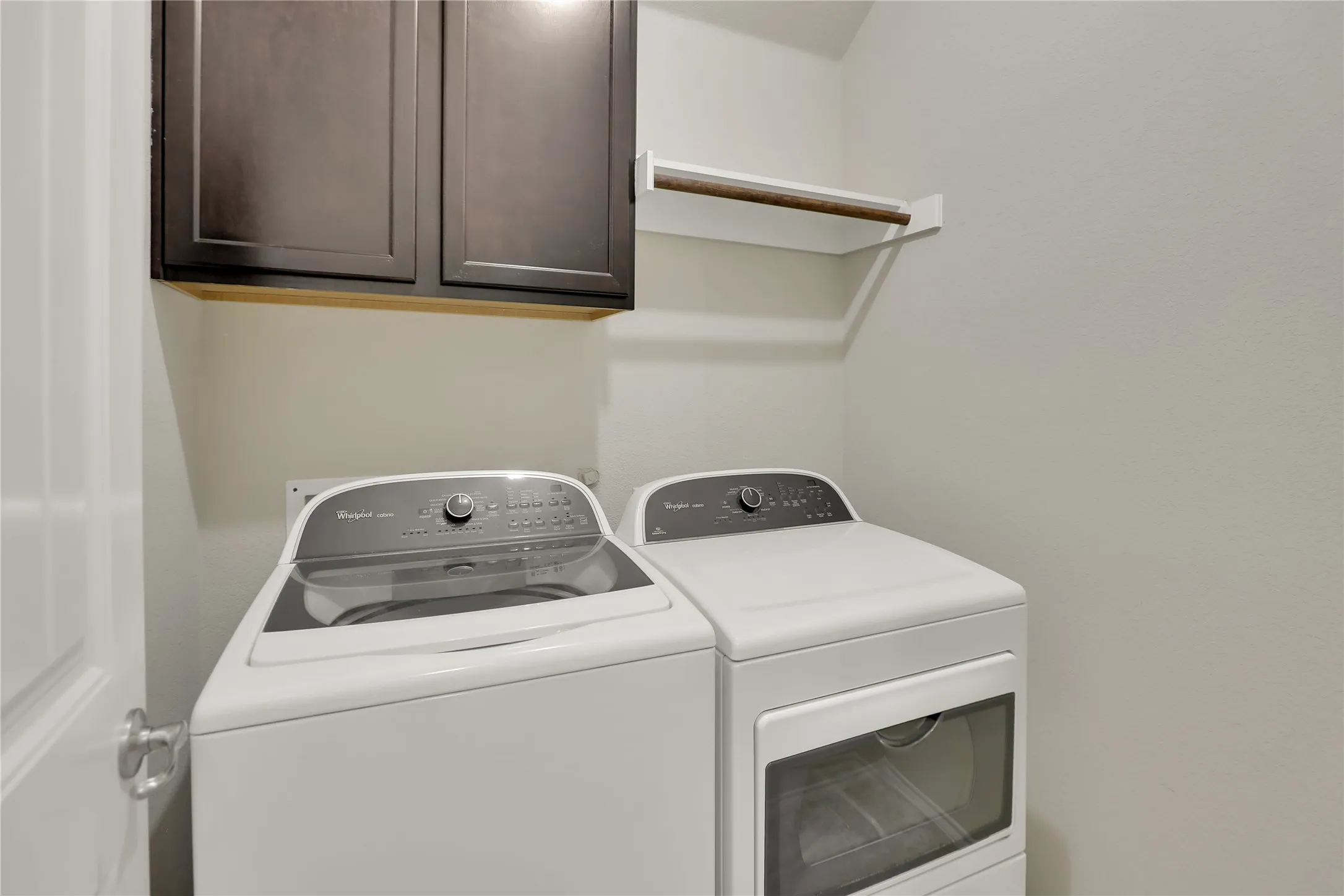Dedicated laundry area featuring overhead dark wood-finish cabinetry, a built-in hanging rod, and light-toned walls
