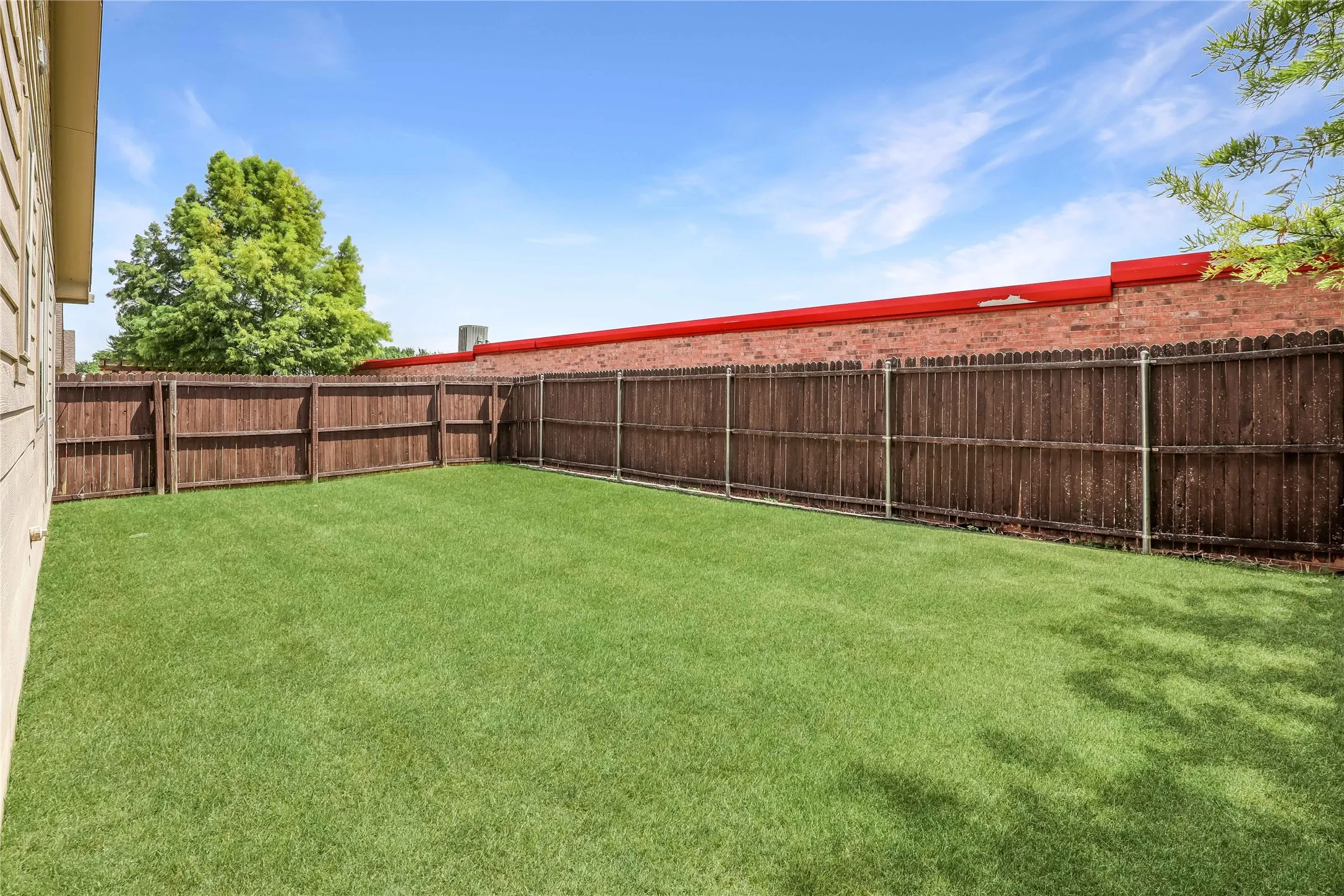 Private backyard space featuring a wooden privacy fence, a verdant lawn, and a light-toned exterior wall
