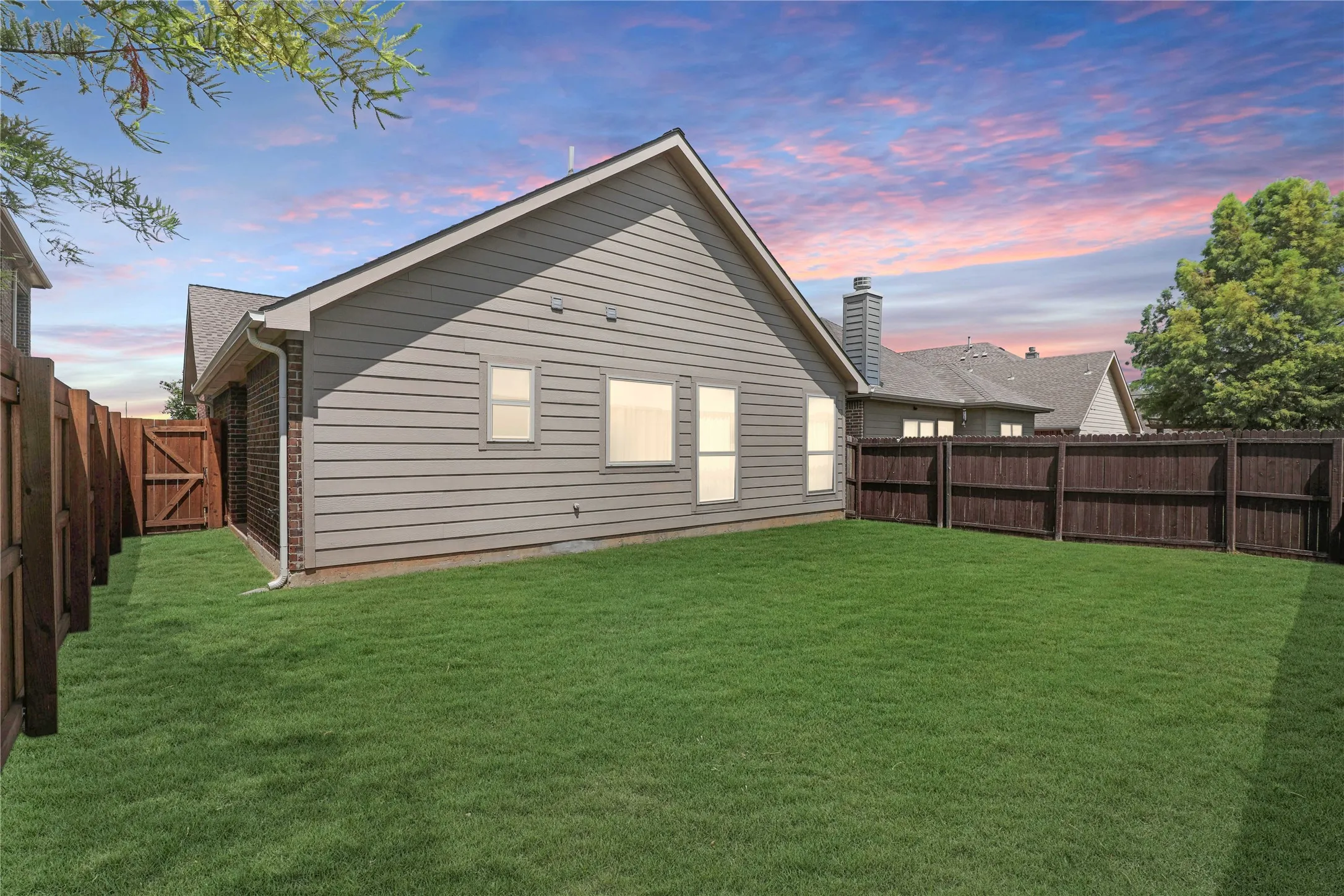 Expansive backyard featuring a manicured lawn, full privacy fencing, and a gray siding exterior with brick accents