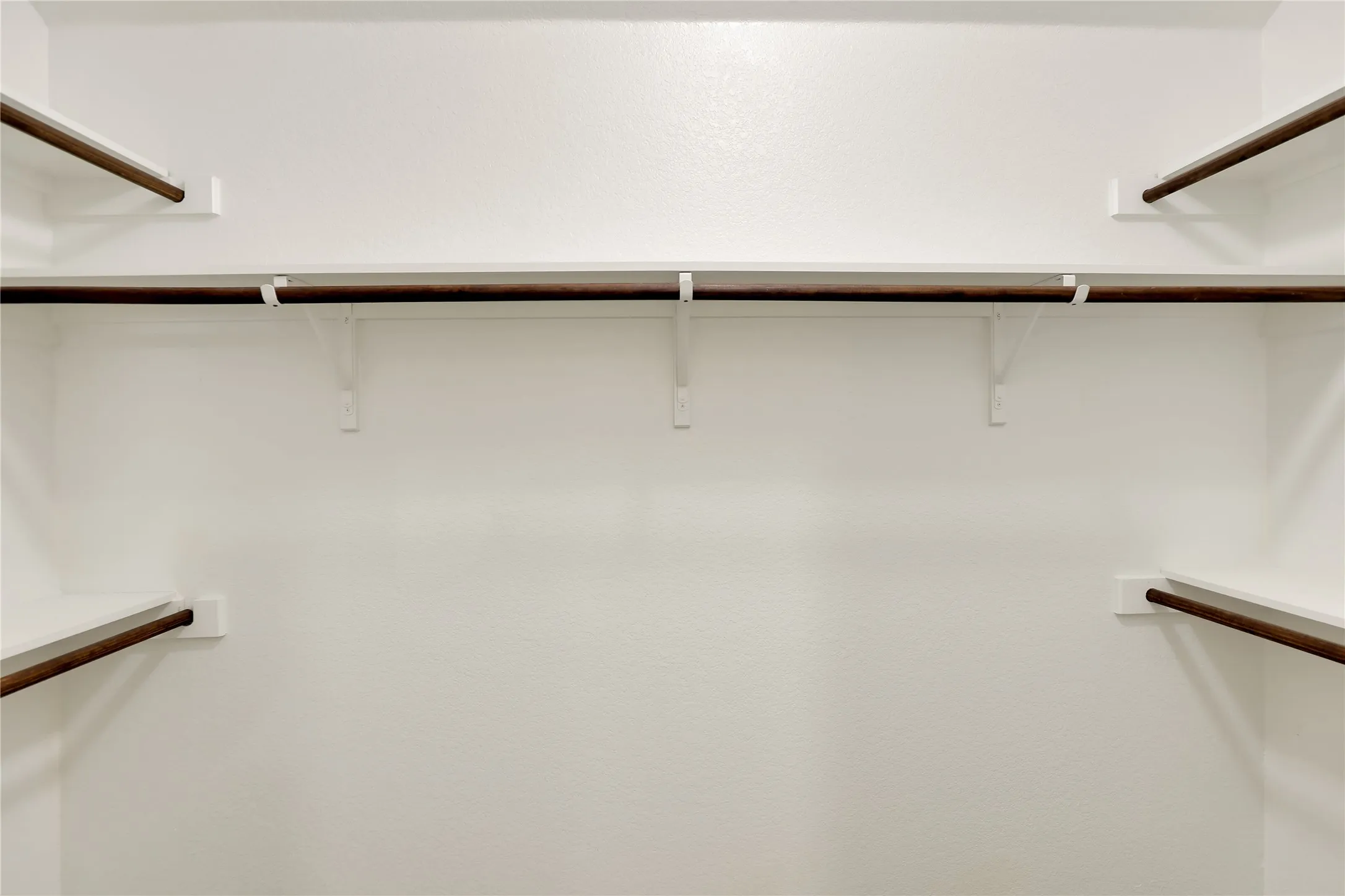 White painted storage area with multiple shelves and dark wood-finish hanging rods