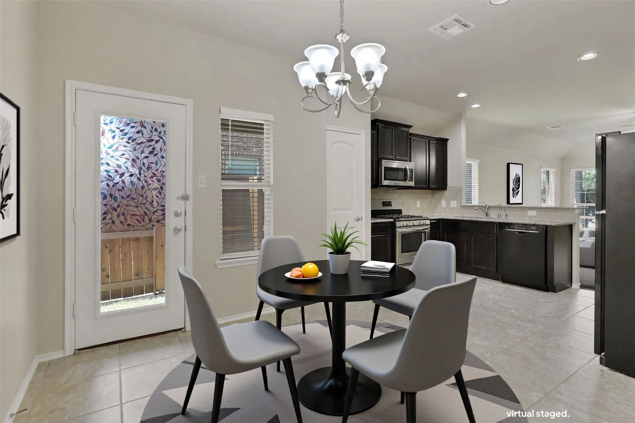 Open-concept kitchen and dining area featuring dark wood-finish cabinetry, stainless steel appliances, and light-toned tile flooring