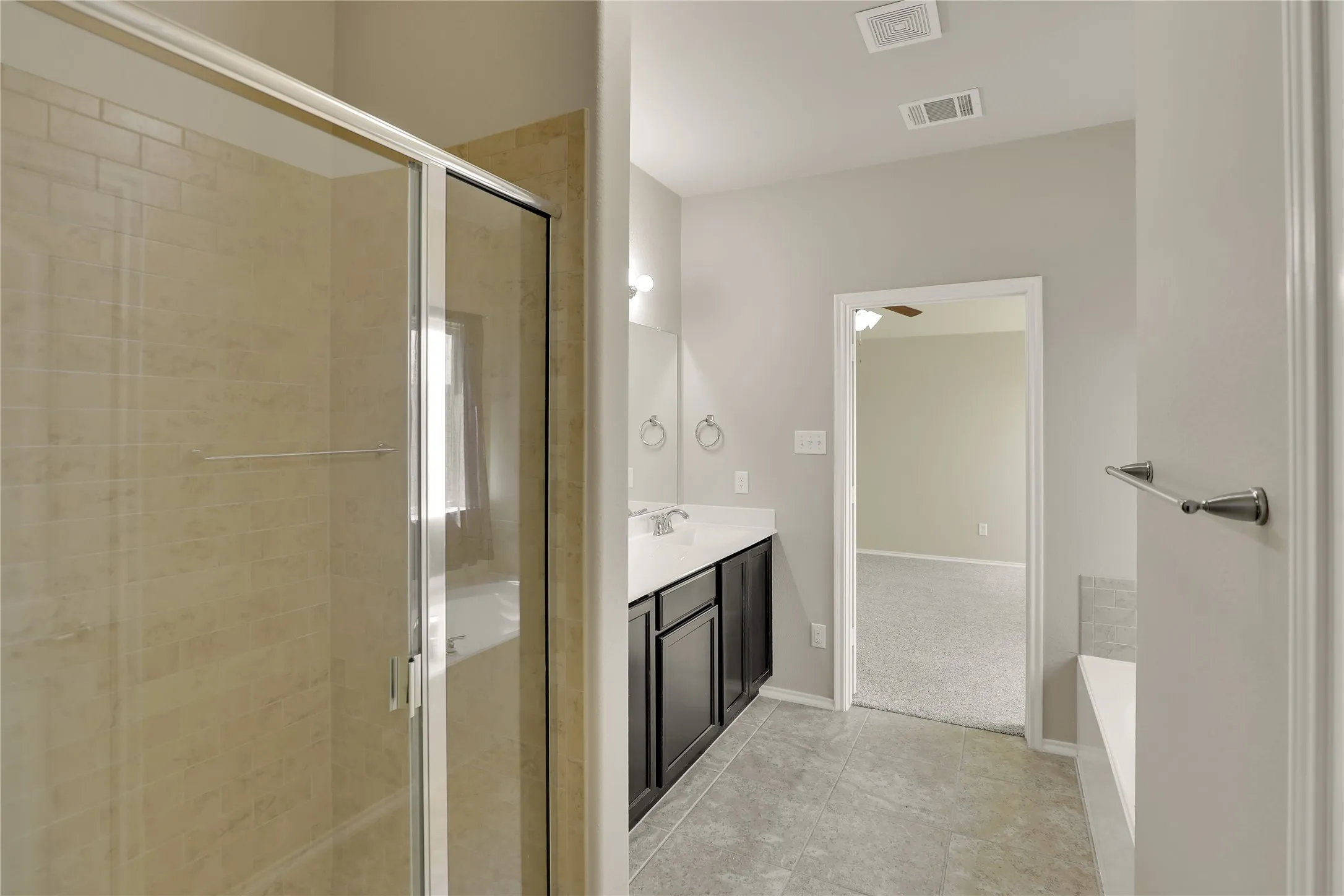 Bathroom featuring a glass-enclosed shower with tile surround, a dark wood-finish vanity with a light-colored countertop, and gray tile flooring