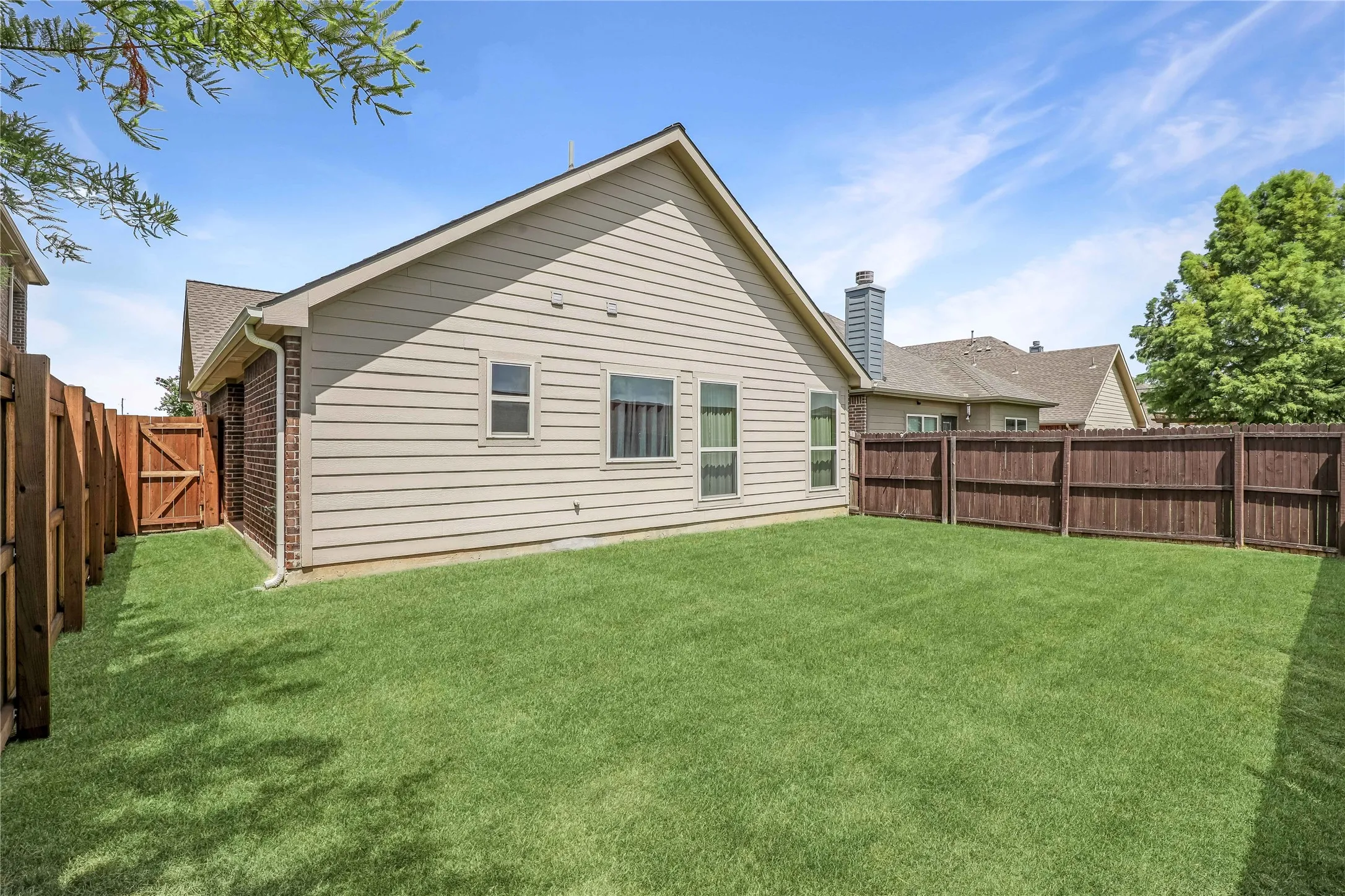Expansive backyard featuring a lush lawn, privacy fencing, and a side access gate