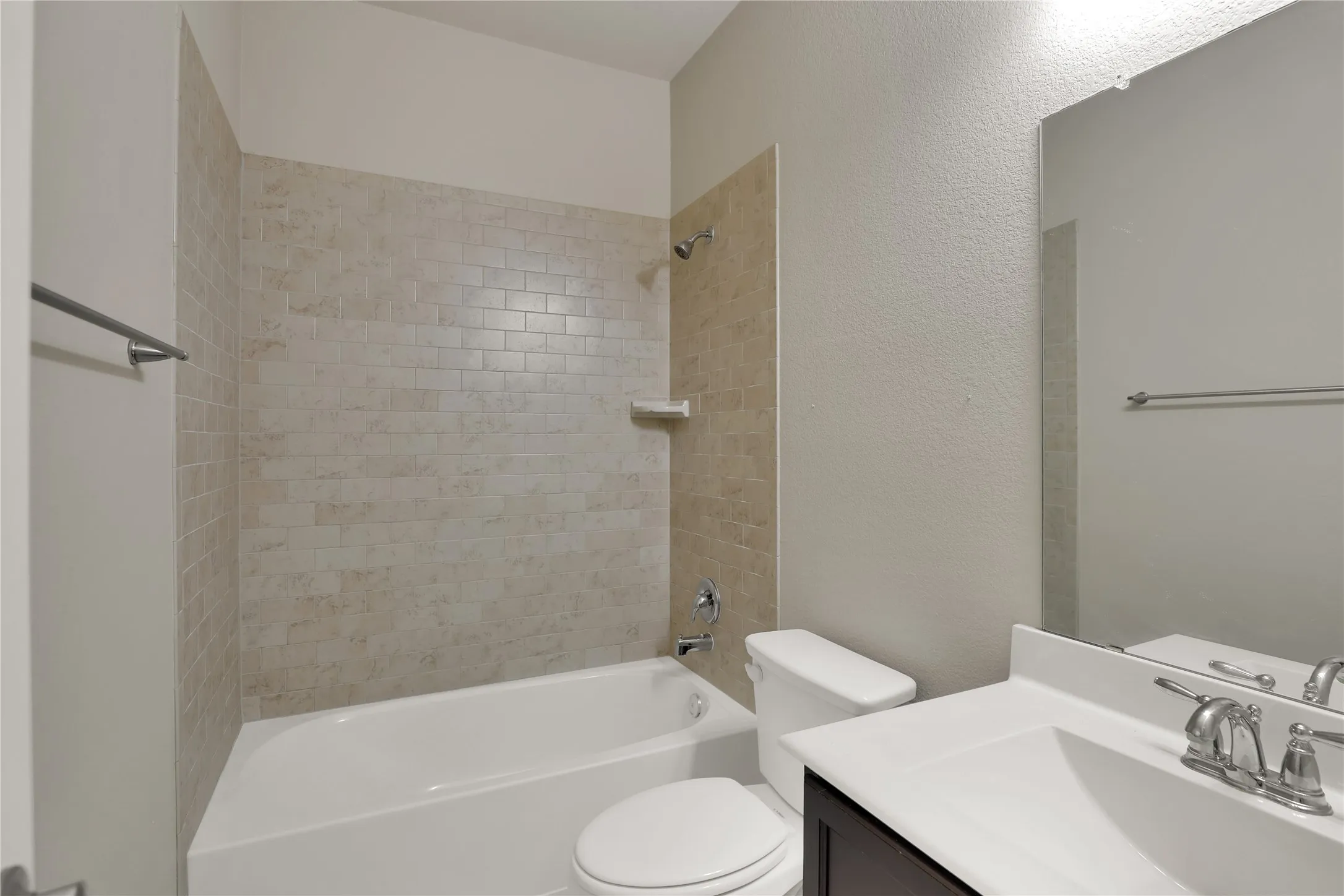 Full bathroom featuring a white tub, subway tile surround, polished chrome fixtures, a dark wood-finish vanity with a white countertop, and a wall-mounted mirror