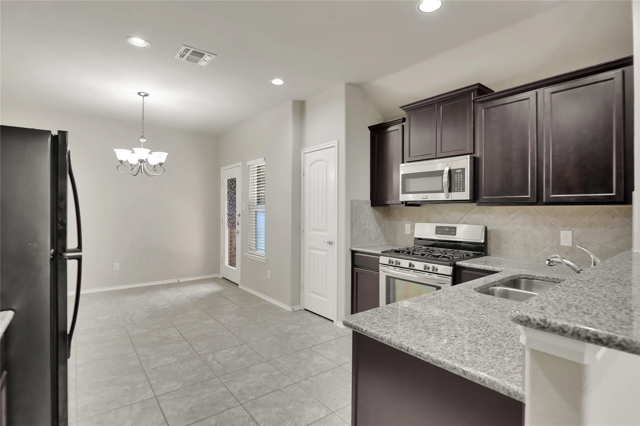 Kitchen featuring dark wood cabinetry, stainless steel appliances, granite countertops, and a tile backsplash