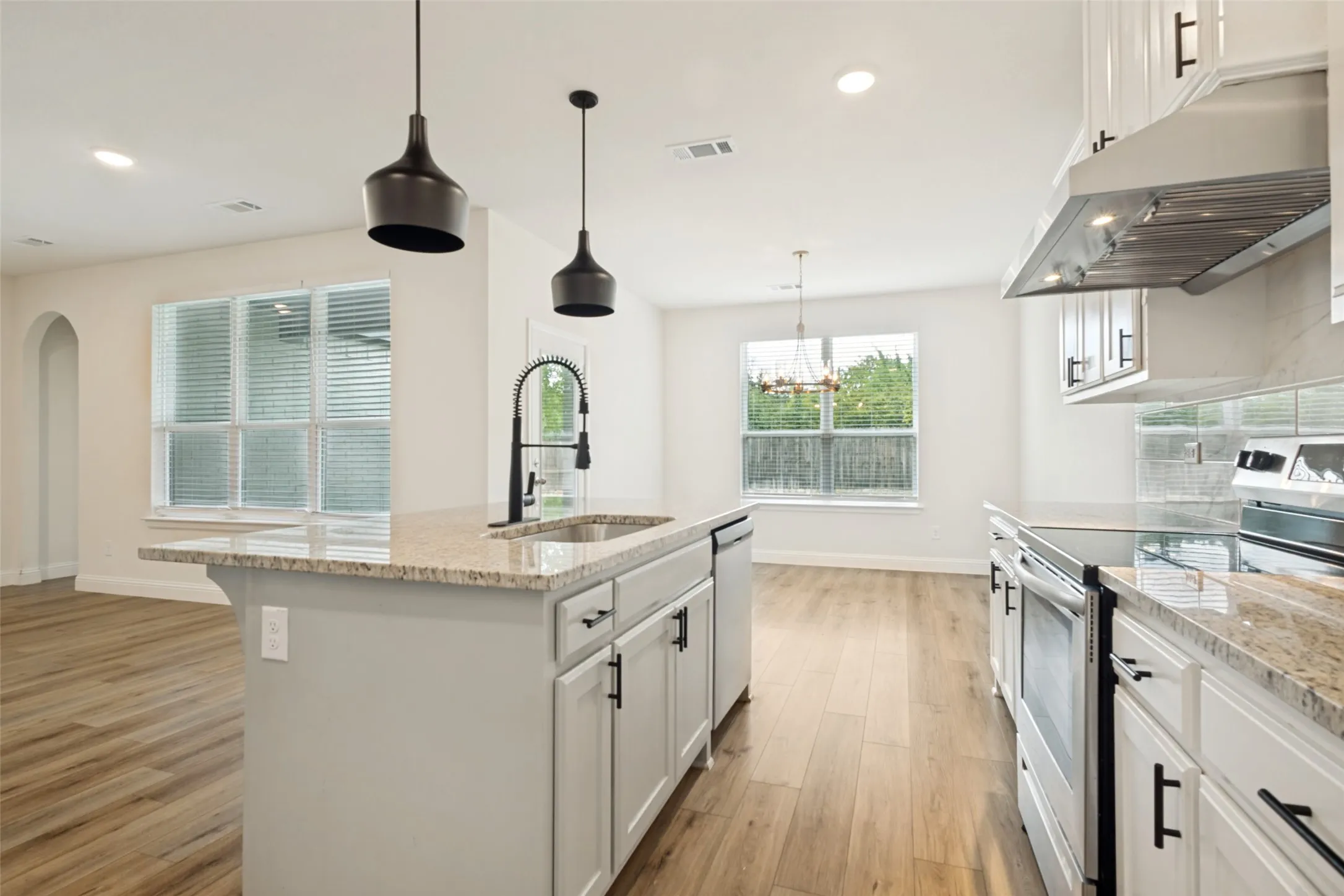 Kitchen featuring an island with an undermount sink and gooseneck faucet, light-colored granite countertops, white cabinetry with matte black hardware, and wood-finish flooring