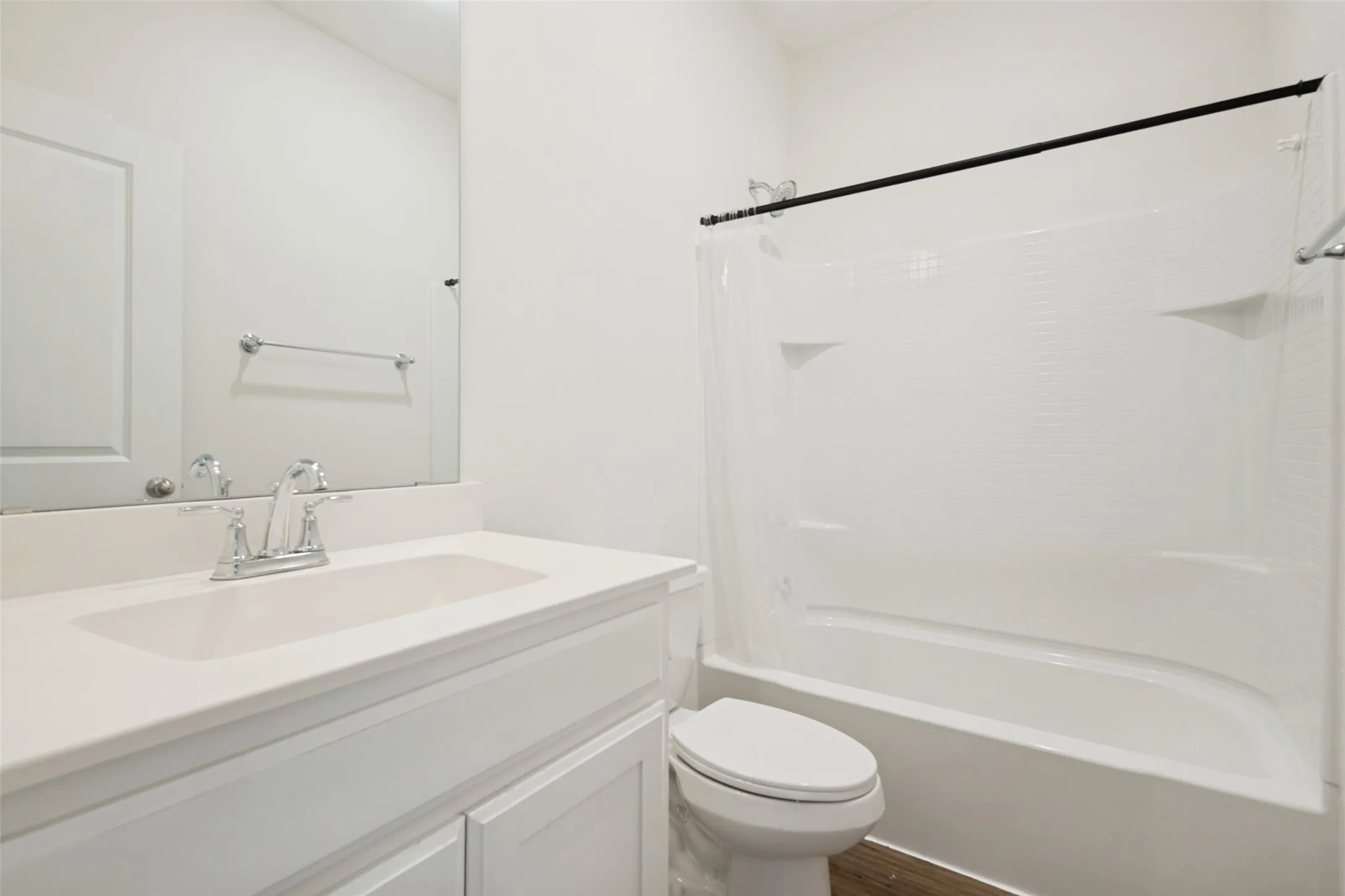 Bathroom featuring a white vanity with an integrated sink, polished chrome faucet, a large wall-mounted mirror, a built-in bathtub with integrated shelving, and wood-finish flooring