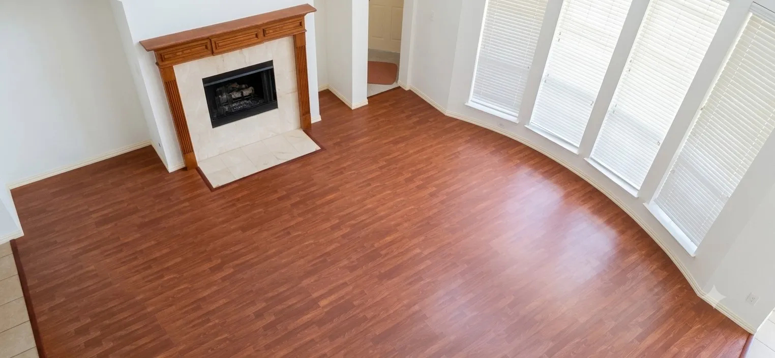 Spacious room featuring wood-finish flooring, a fireplace with a wood mantel and stone surround, and a curved wall with multiple windows fitted with blinds