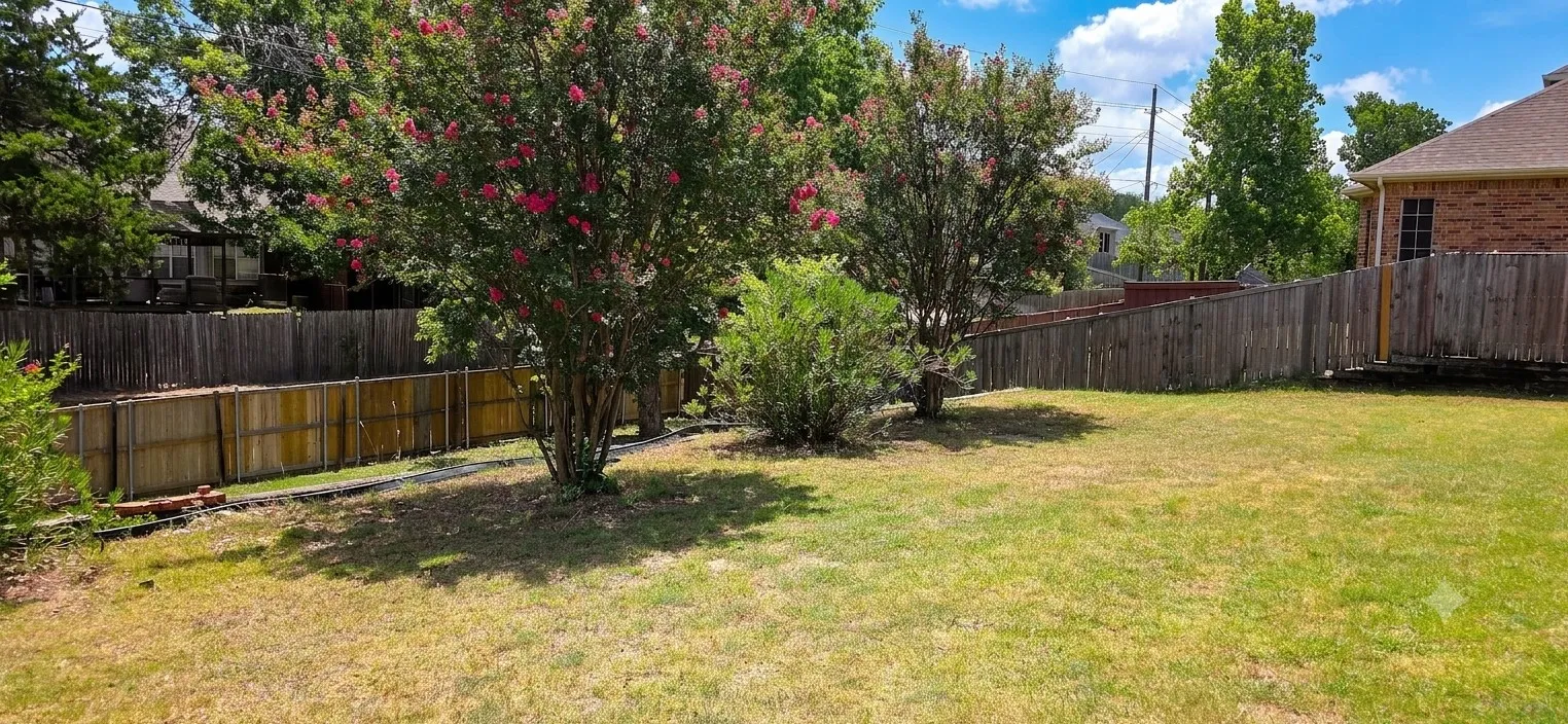 Expansive backyard featuring a lush lawn, two mature trees with red blossoms, and a wood privacy fence