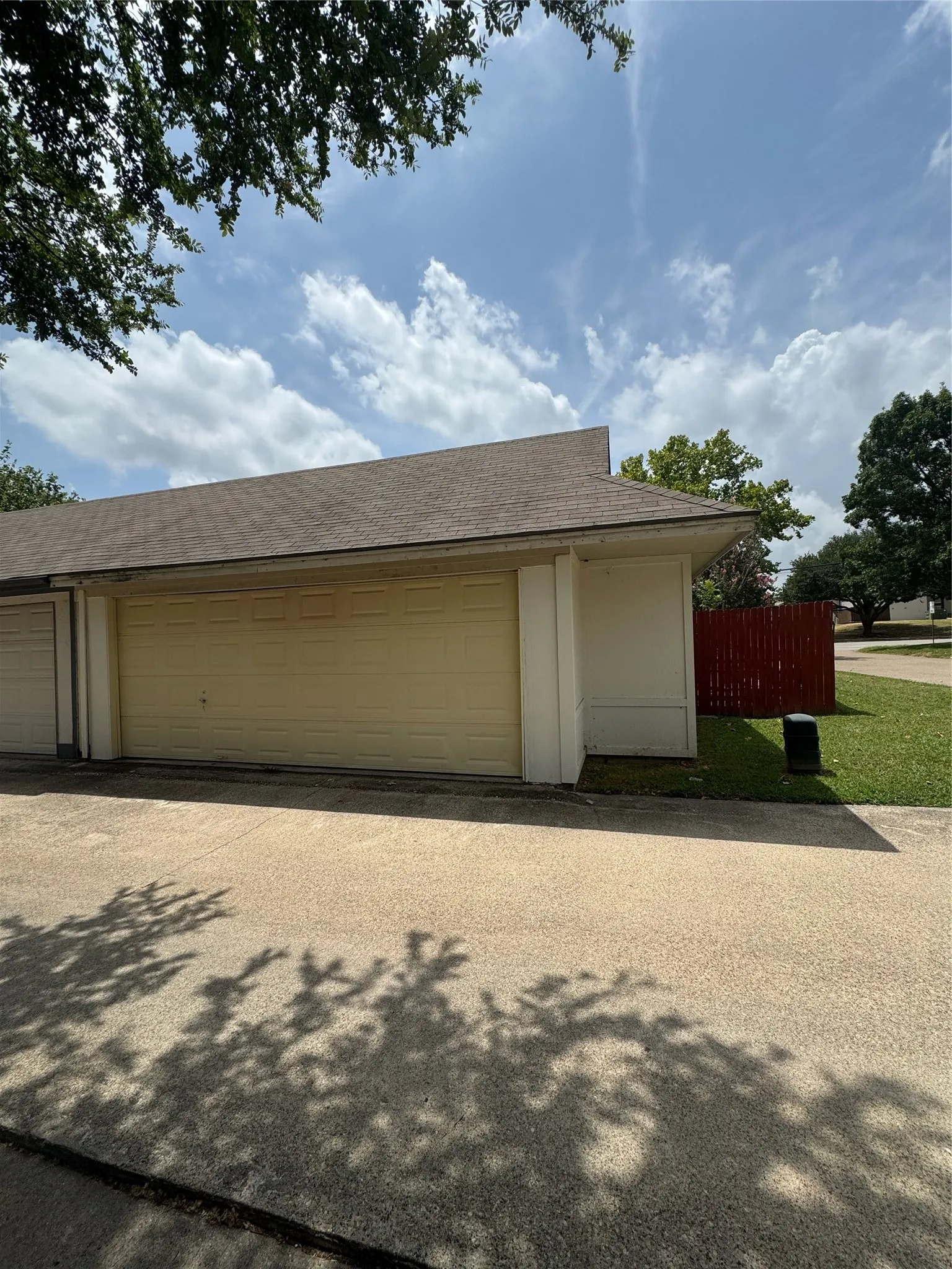 Attached multi-car garage with light-colored garage doors, a shingle roof, and a concrete drive