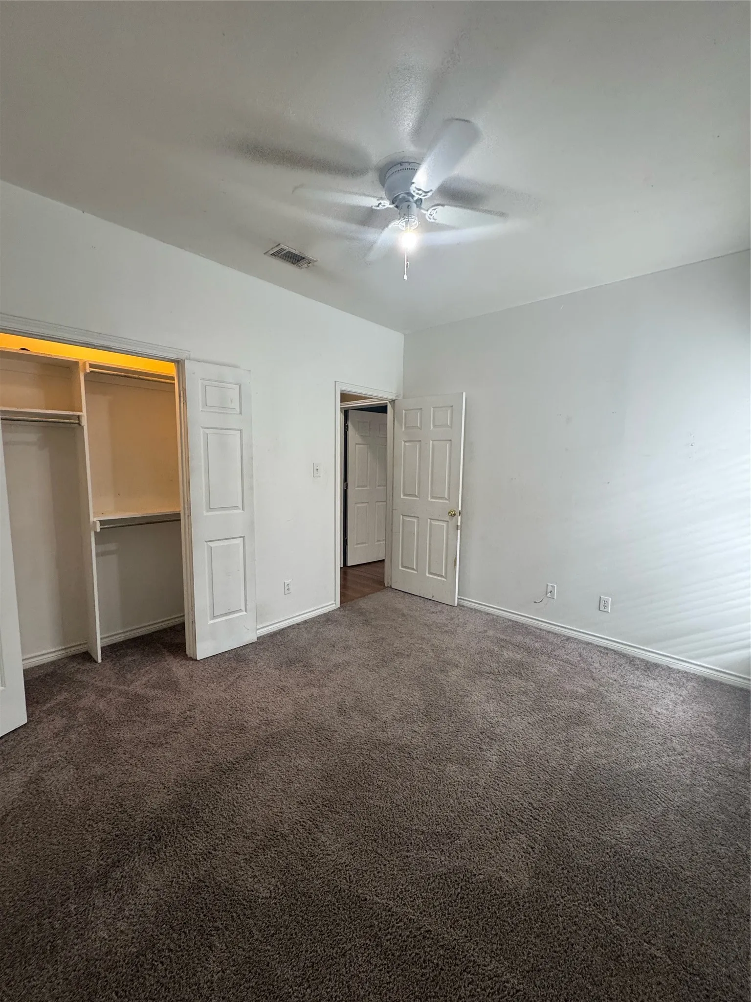 Carpeted room featuring a ceiling fan with integrated lighting, white baseboards, and a built-in closet with shelving