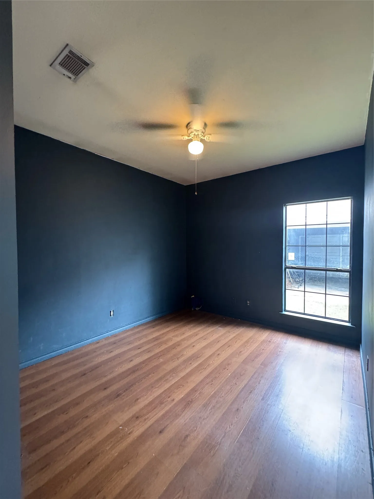 Spacious room featuring wood-finish flooring, dark-toned walls, and a multi-pane window