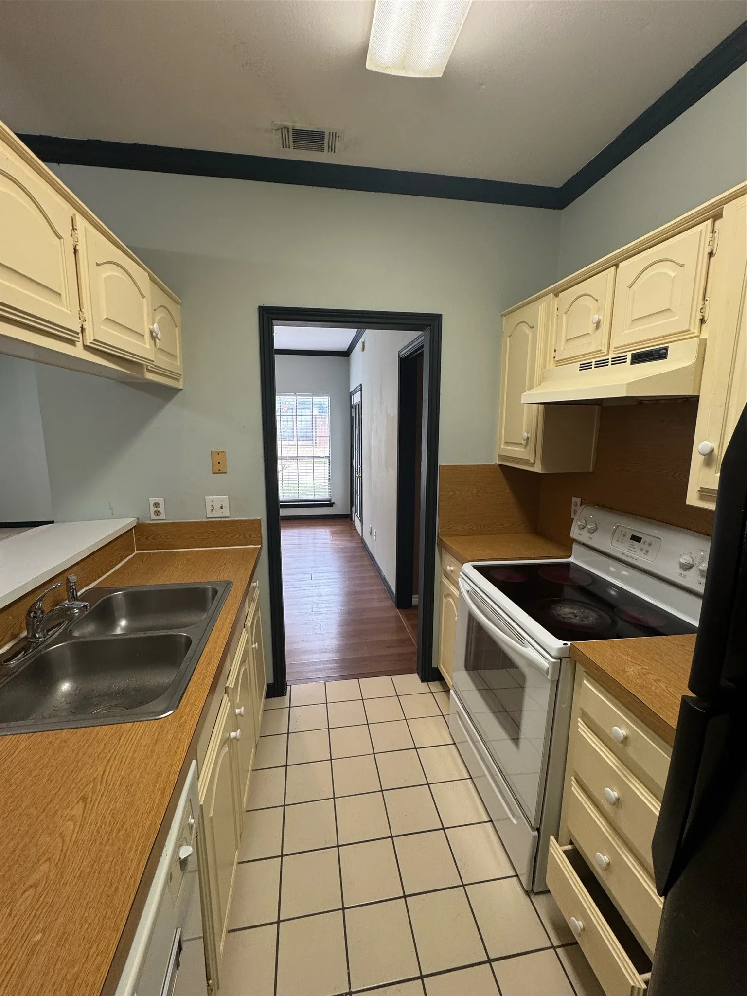 Galley-style kitchen featuring cream cabinetry, wood-finish countertops, and a double basin stainless steel sink