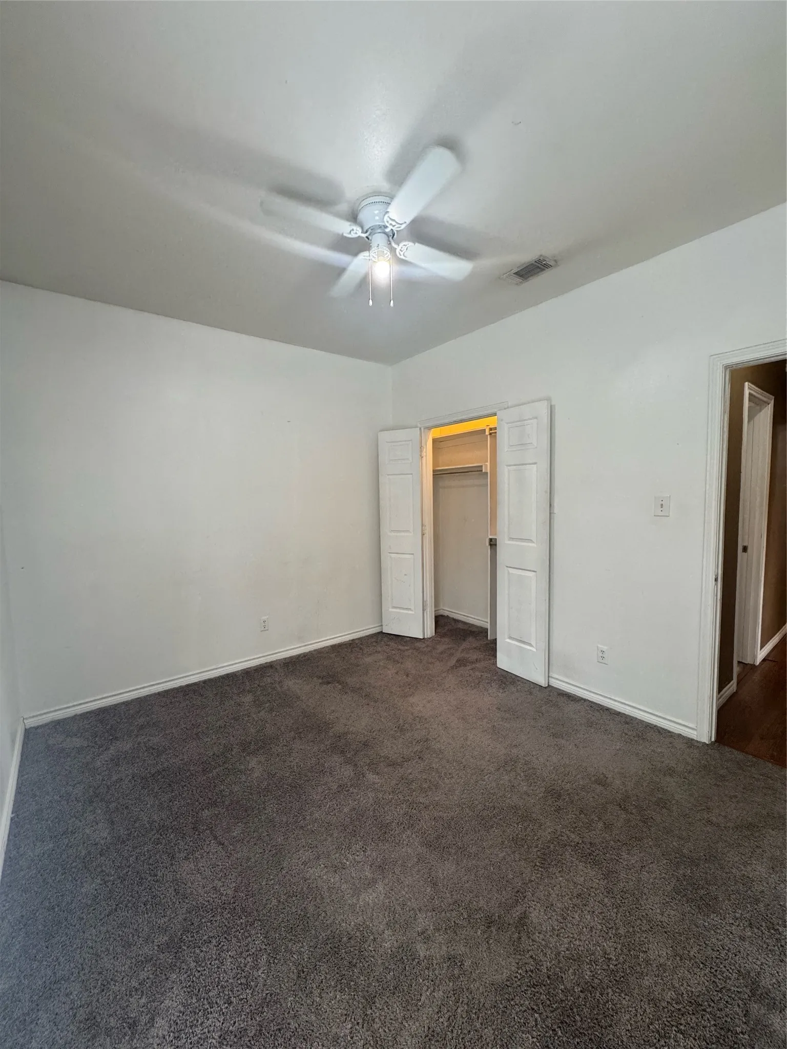 Spacious room featuring neutral carpeting, white walls, and a ceiling fan with integrated lighting